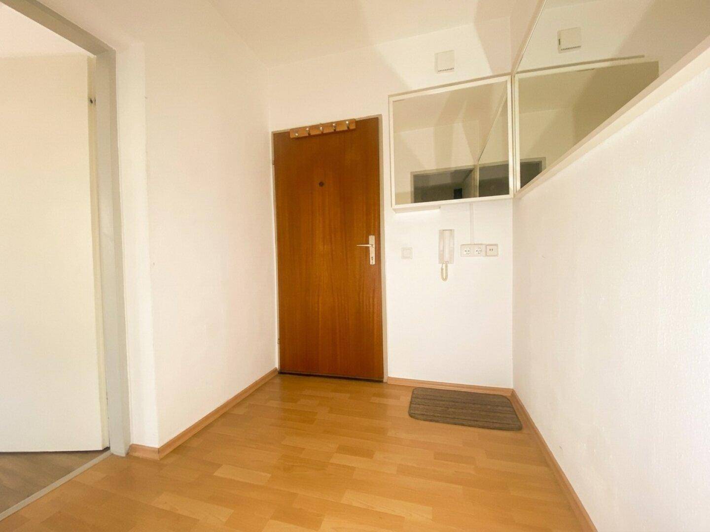 Heller Eingangsbereich mit Holztür, Laminatboden und Gegensprechanlage.