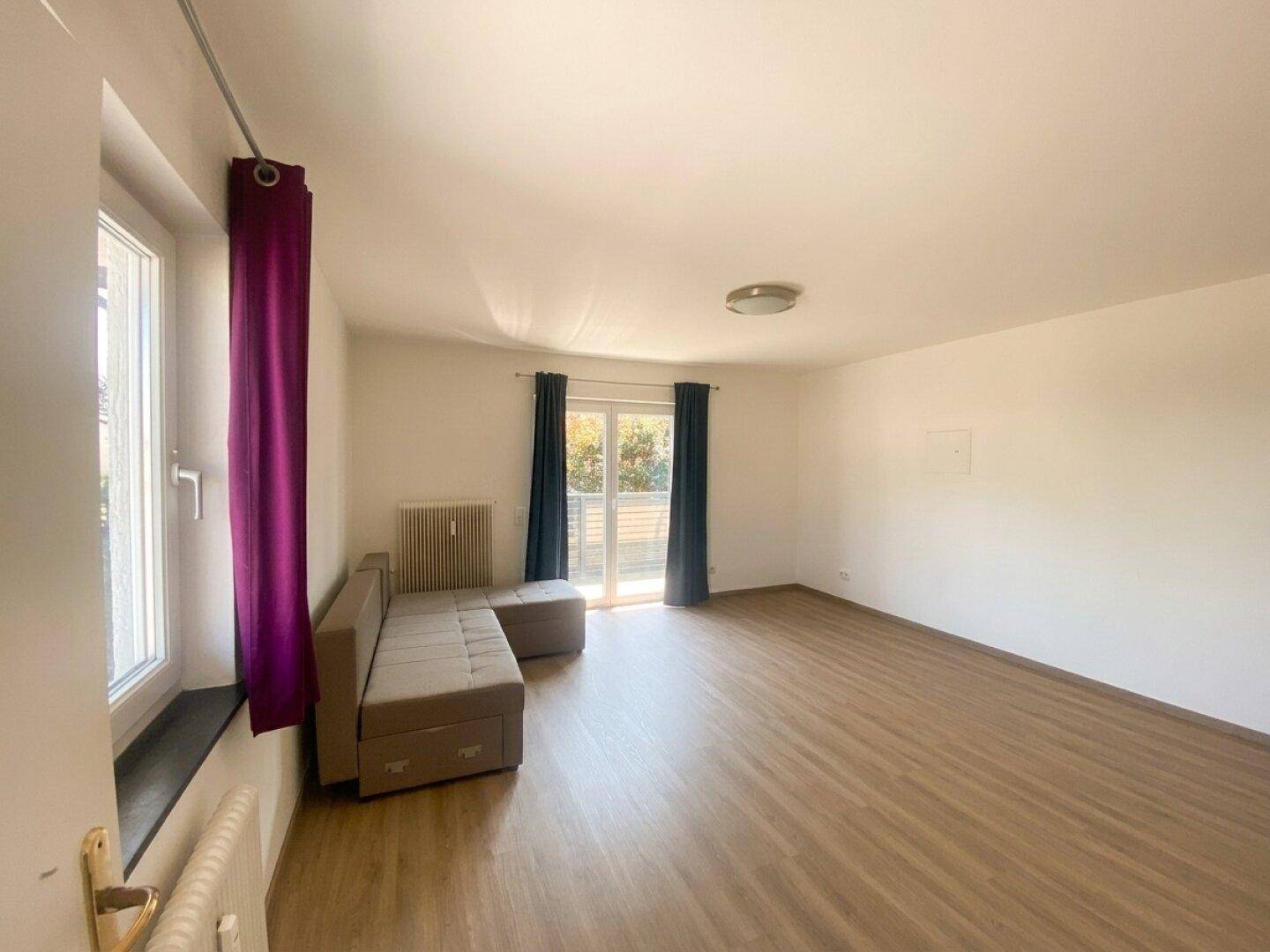 Geräumiges Wohnzimmer mit Laminatboden, Sofa und Zugang zu einem Balkon.