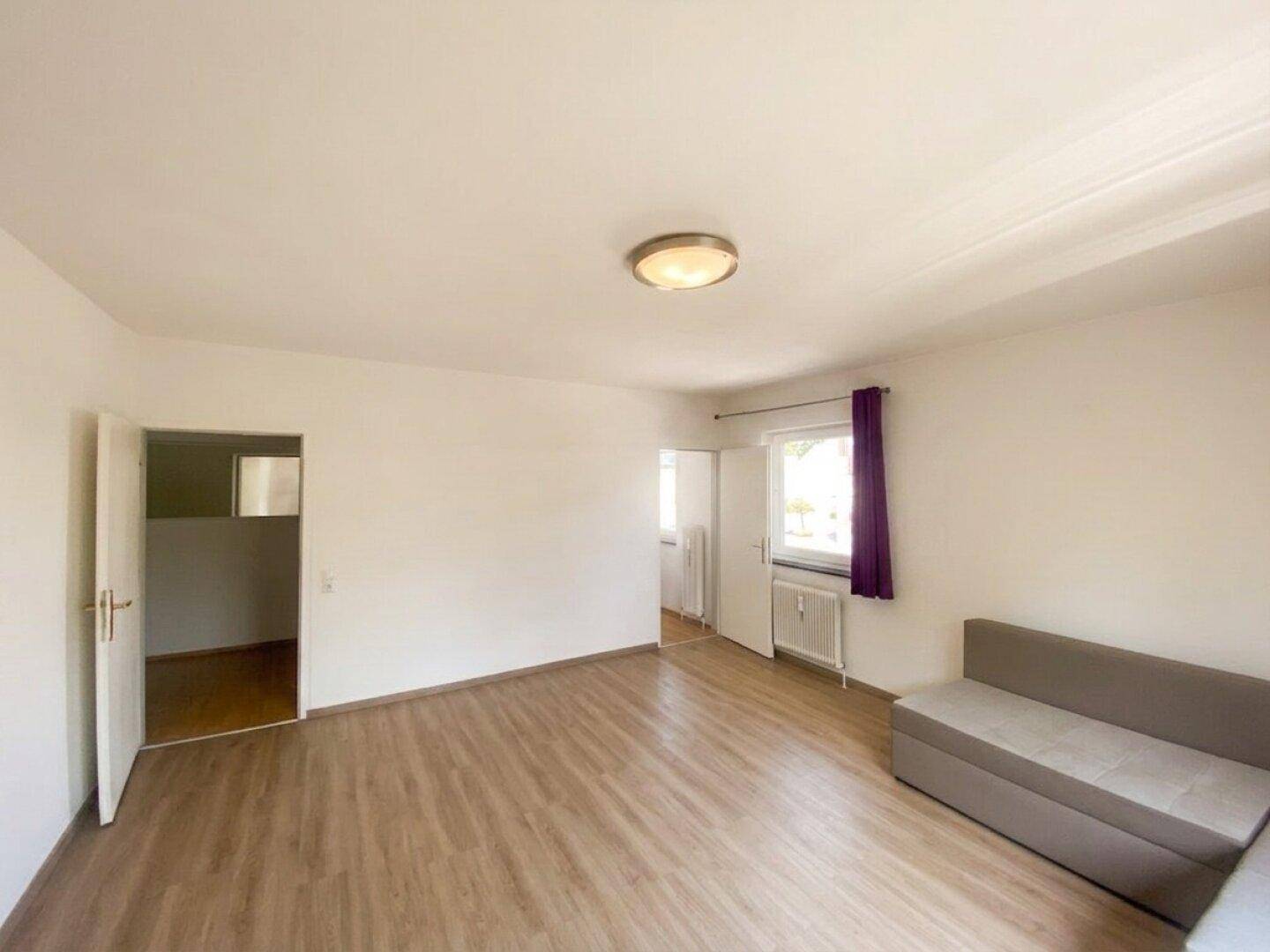 Helles Wohnzimmer mit Laminatboden und Zugang zu weiteren Räumen.
