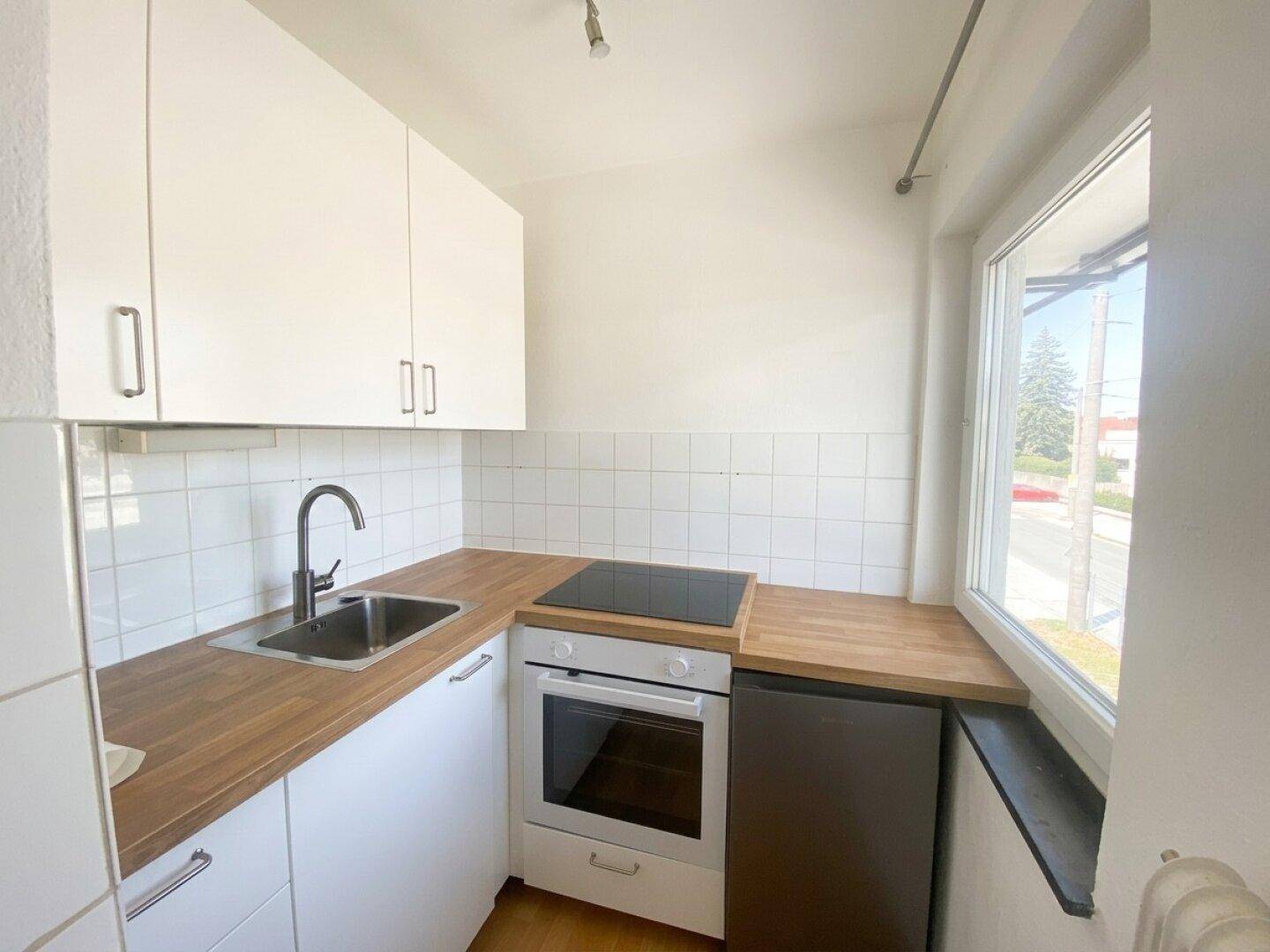 Kleine, helle Küche mit weißen Schränken, Holz-Arbeitsplatten und Fenster.