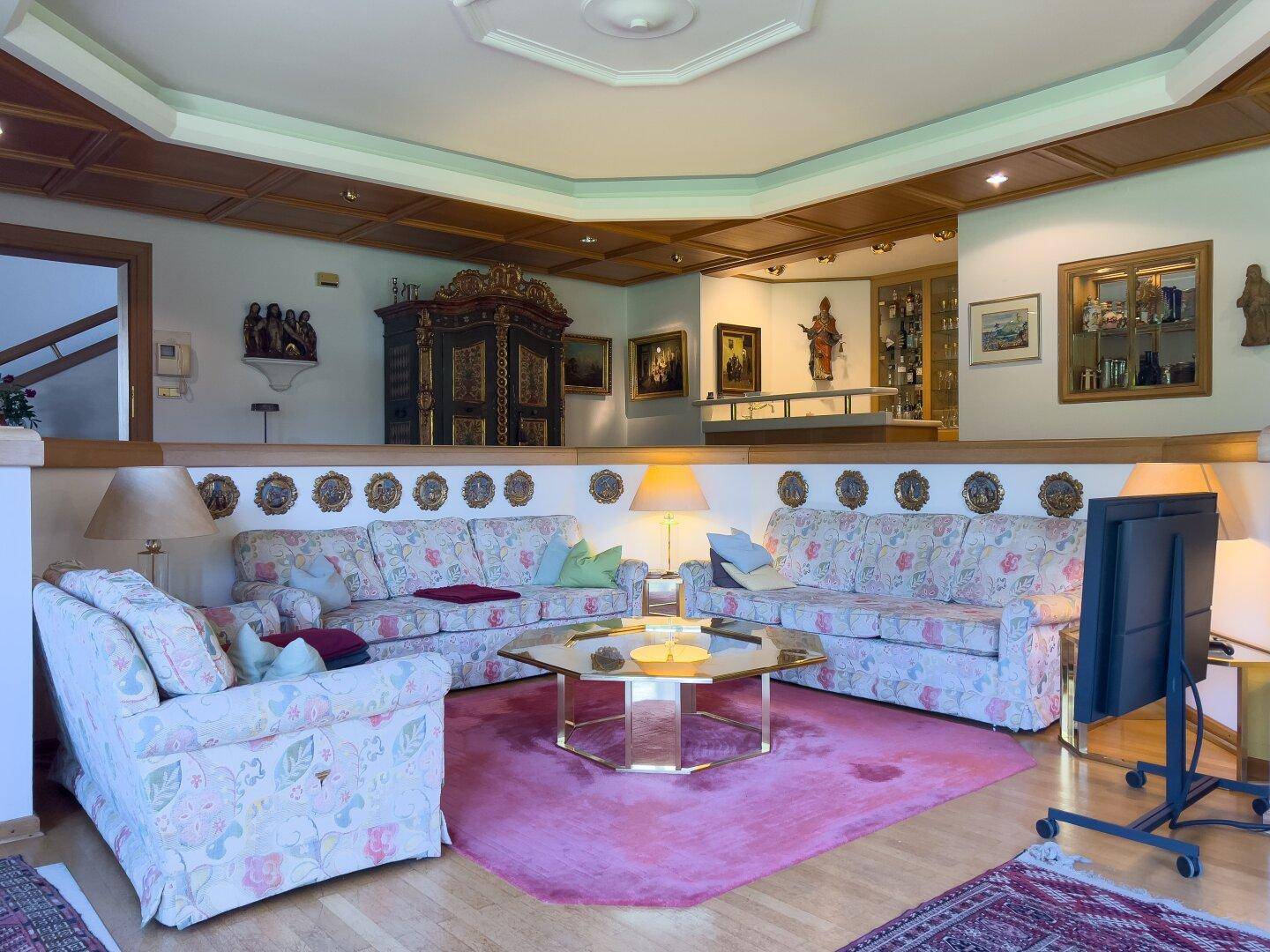 Geräumiges Wohnzimmer mit floralen Sofas, Holzbalkendecke und traditionellen Möbeln auf zwei Ebenen.