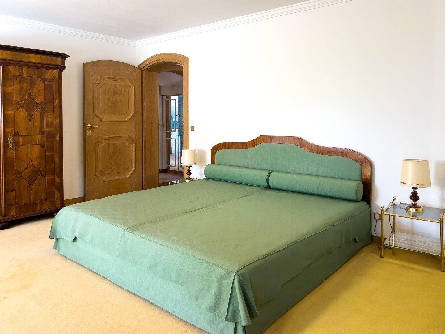 Helles Schlafzimmer mit grünem Bett, gelbem Teppichboden und Holztüren.