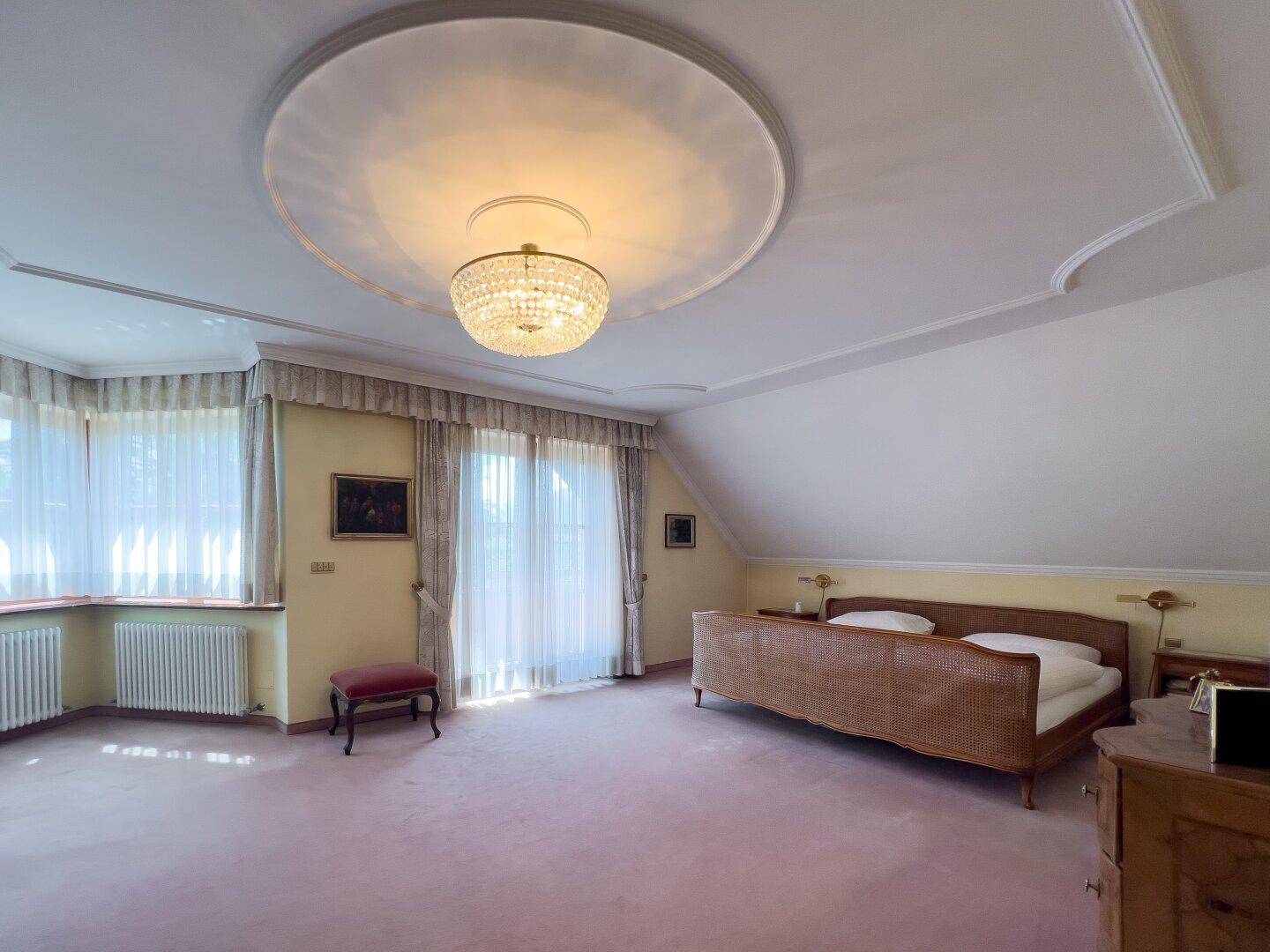 Geräumiges Schlafzimmer mit rosa Teppichboden, Doppelbett und Zugang zu einem Balkon.