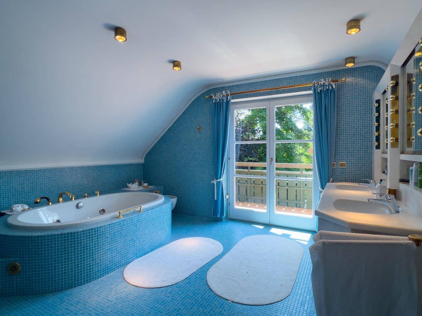Blau gefliestes Badezimmer mit Whirlpool-Badewanne, Doppelwaschbecken und Balkonzugang.