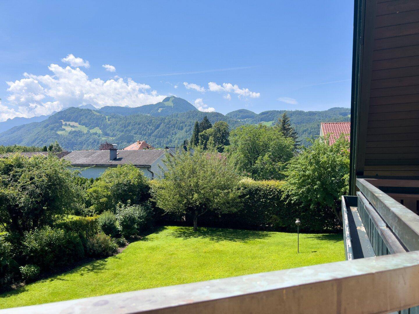 Panoramablick auf grüne Berge und Gärten von einem Balkon aus.