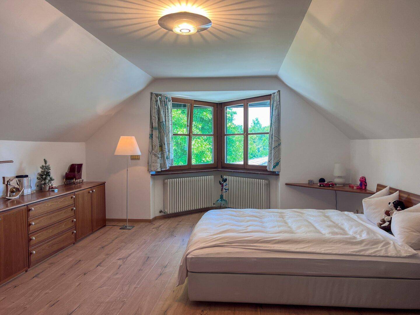 Gemütliches Schlafzimmer im Dachgeschoss mit Holzboden, Erkerfenster und Blick ins Grüne.
