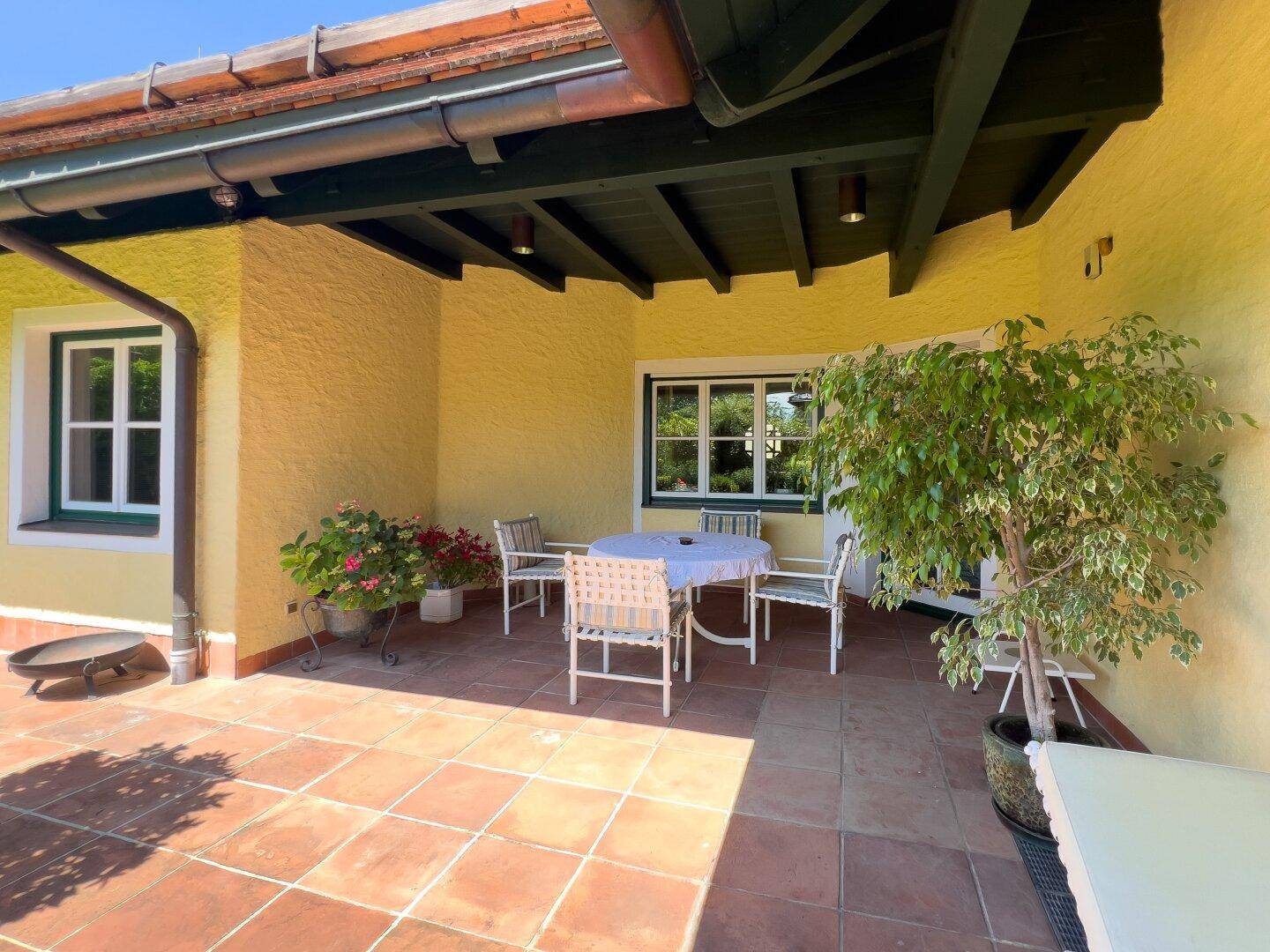 Überdachte Terrasse mit Terrakotta-Fliesen, Gartenmöbeln und Pflanzen.