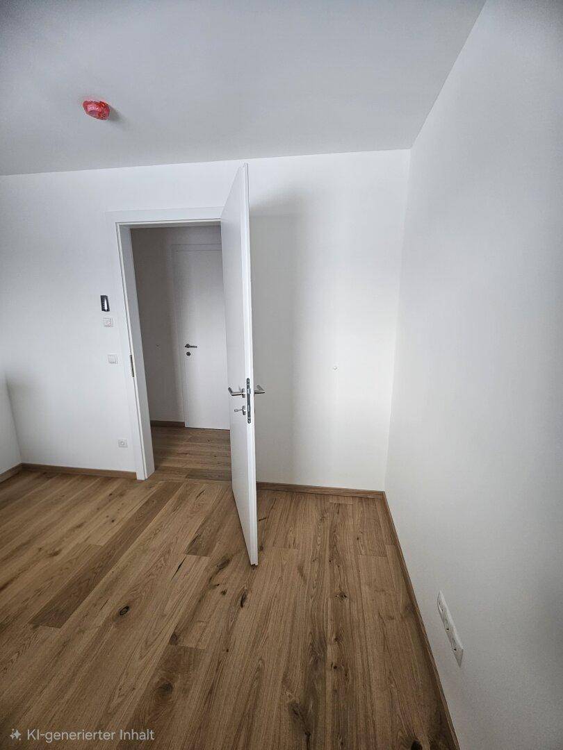 Heller Raum mit Holzparkett und weiß gestrichenen Wänden, eine offene Tür führt in den Flur.
