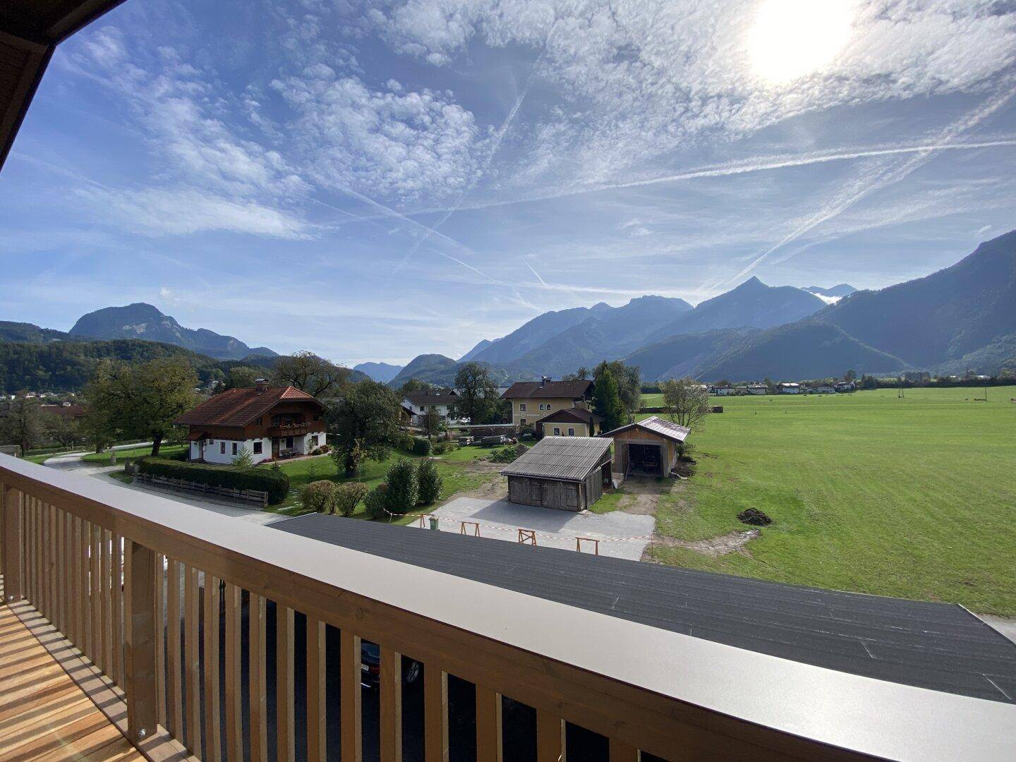Sonniger Balkon mit weitem Blick über die grüne Landschaft und majestätische Berge unter blauem Himmel.