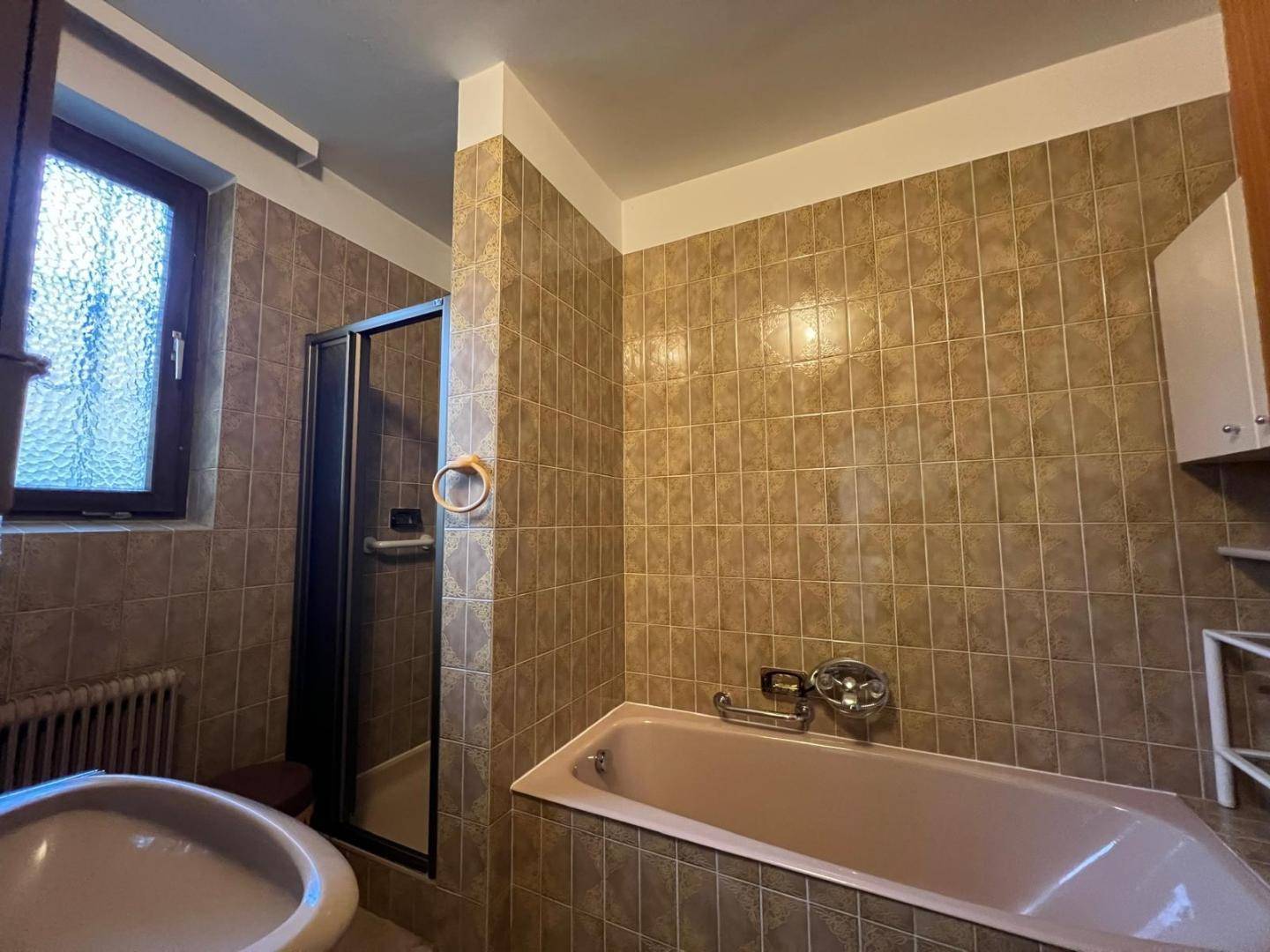 Badezimmer im Stil der 80er Jahre mit braunen Fliesen, rosa Badewanne und Duschkabine.