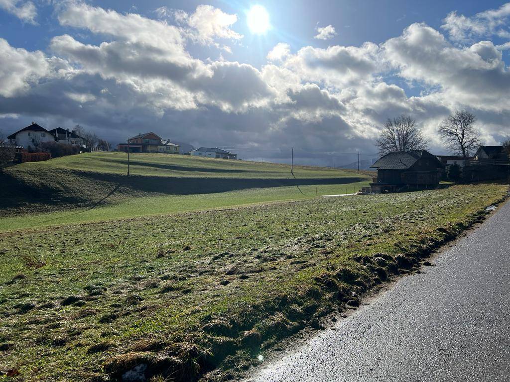 Sonnige Landschaft mit grünen Hügeln, vereinzelten Häusern und einem alten Holzschuppen.