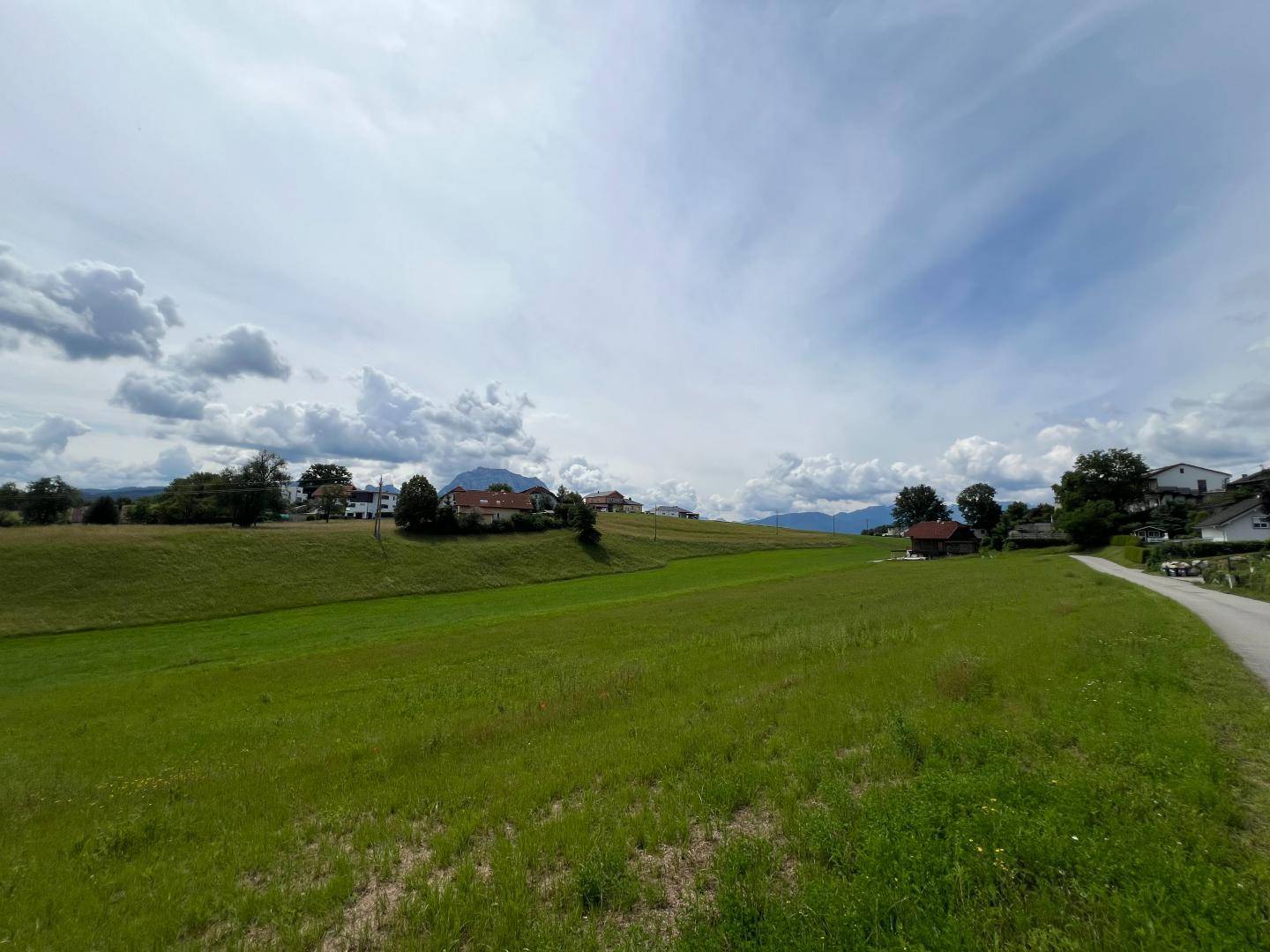 Idyllische grüne Landschaft unter einem weiten Himmel mit Blick auf ferne Berge und Häuser.