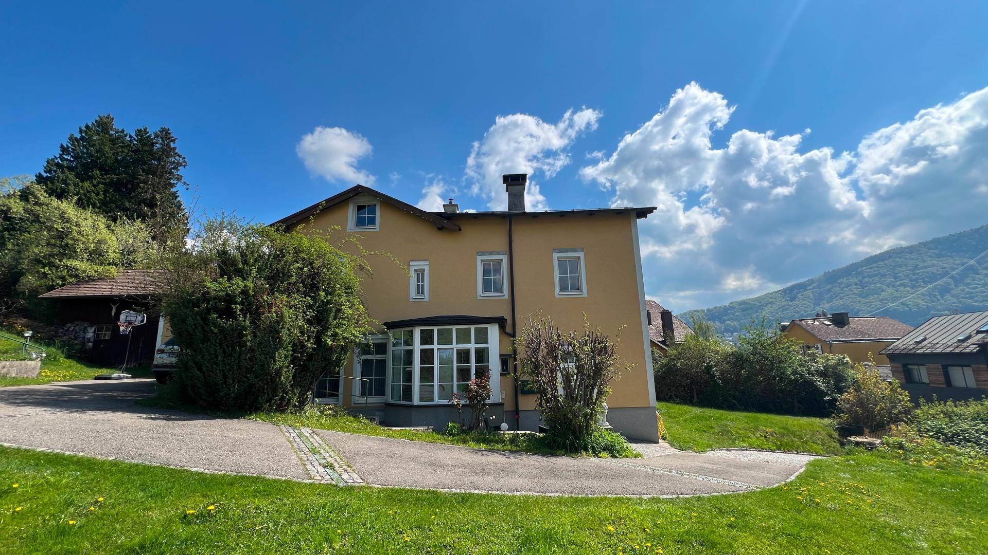 Gelbes Haus mit Erkerfenster und Blick auf die umliegende Berglandschaft unter blauem Himmel.