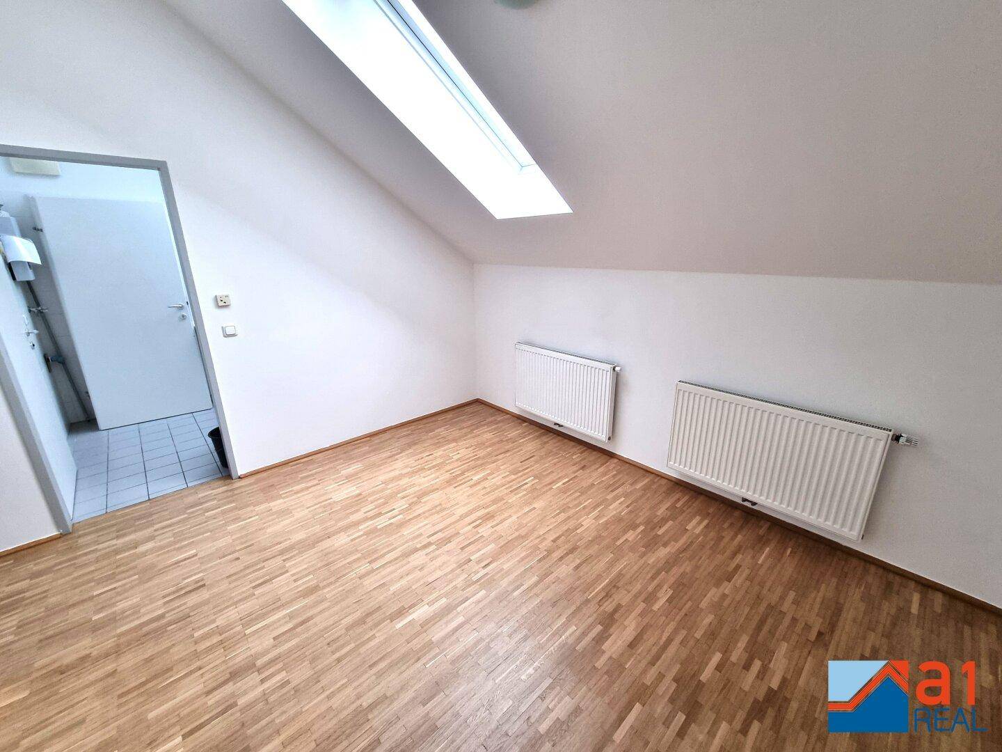 Geräumiger Dachbodenraum mit Holzboden, Dachfenster und Zugang zu einem Nebenraum.