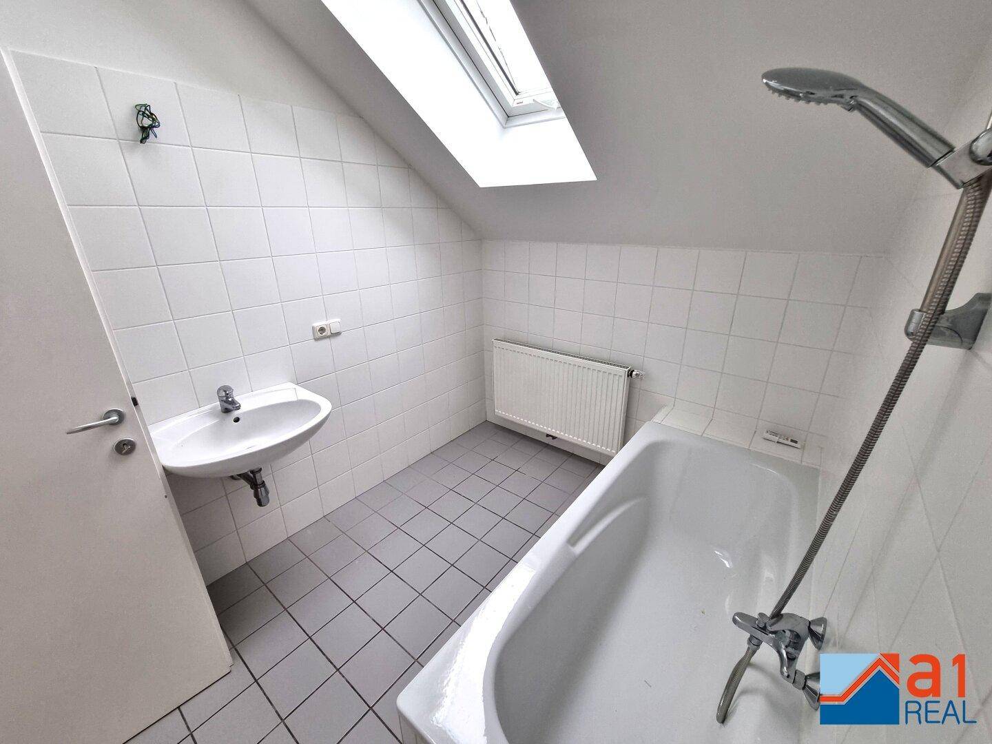 Badezimmer im Dachgeschoss mit Badewanne, Waschbecken und Dachfenster, komplett gefliest.