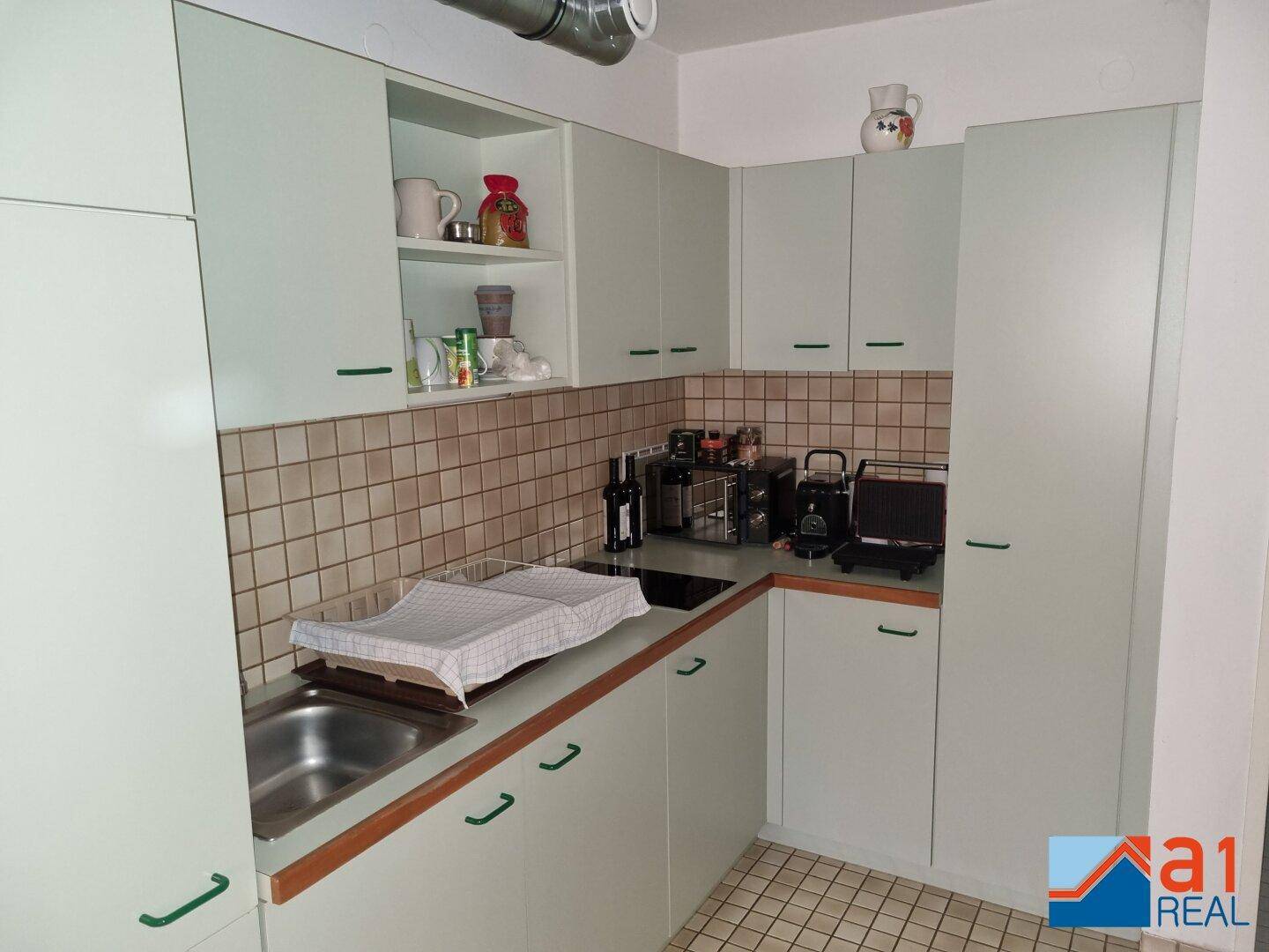 Funktionale Küche mit hellgrünen Schränken, gefliestem Spritzschutz und praktischen Arbeitsflächen.