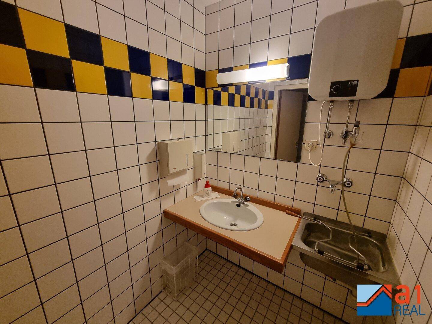 Gefliestes Badezimmer mit Waschbecken, Spülbecken und einem markanten blau-gelben Fliesenmuster.