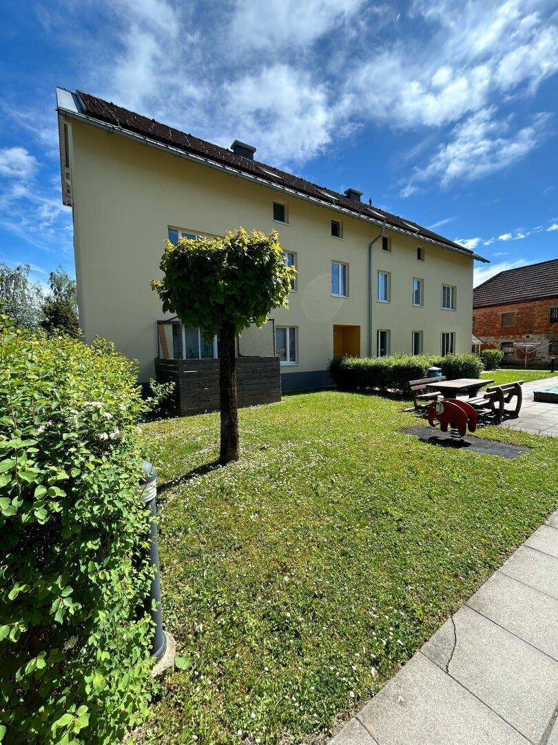 Außenansicht eines Mehrfamilienhauses mit gepflegtem Garten und kleinem Spielplatzbereich.