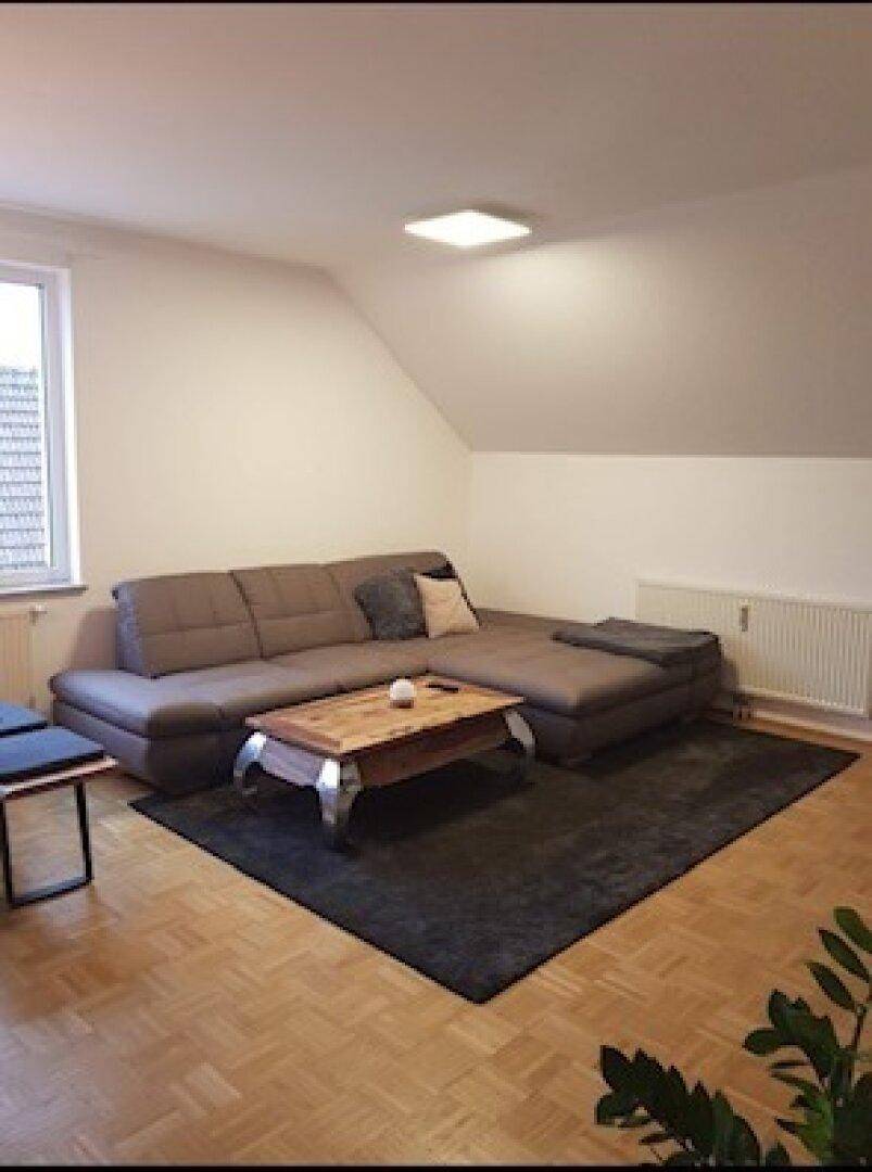 Gemütliches Wohnzimmer mit Dachschräge, Parkettboden und großem Ecksofa.