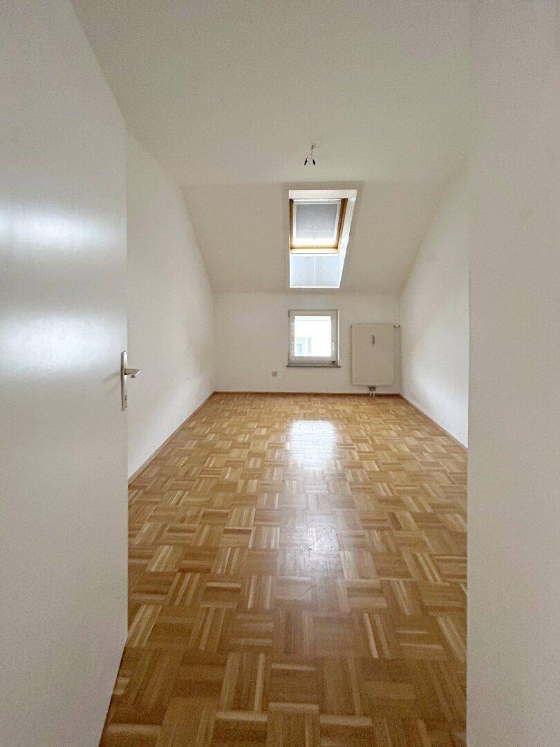 Helles Zimmer im Dachgeschoss mit Parkettboden, Dachschräge und Oberlichtfenster.
