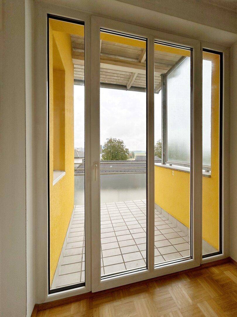 Heller Balkon mit Fliesenboden und gelben Wänden, zugänglich durch eine Glasschiebetür.