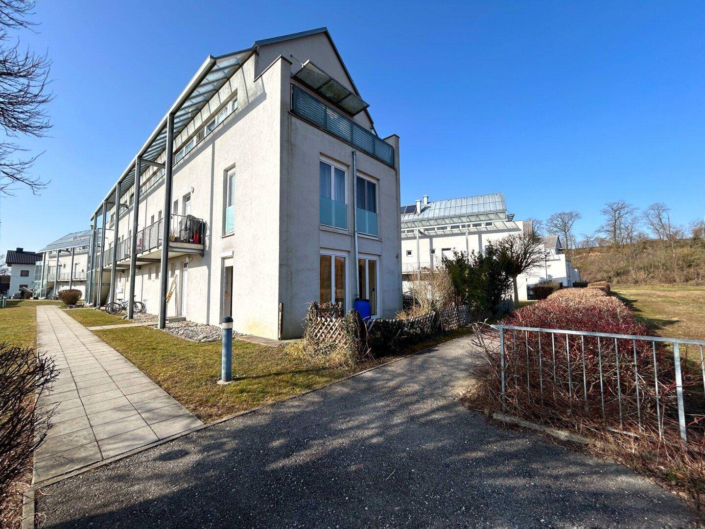 Ansicht des modernen Mehrfamilienhauses von der Seite mit Gehwegen und Grünflächen.