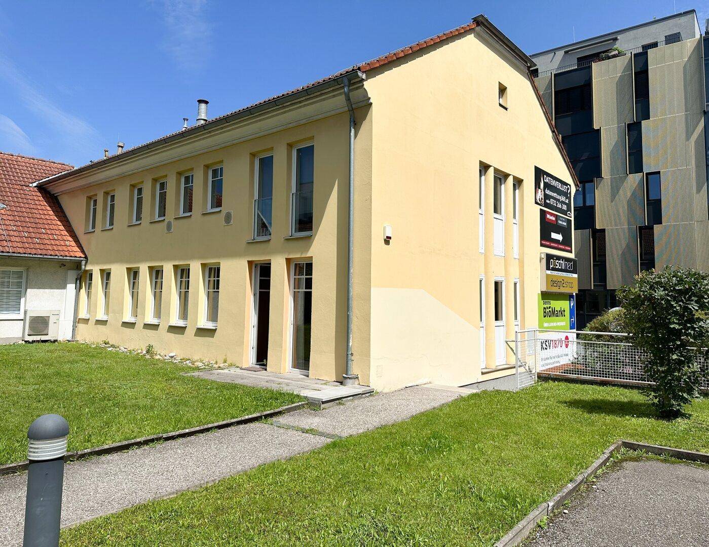 Gelbes Geschäftsgebäude mit mehreren Fenstern und einem modernen Nachbargebäude.
