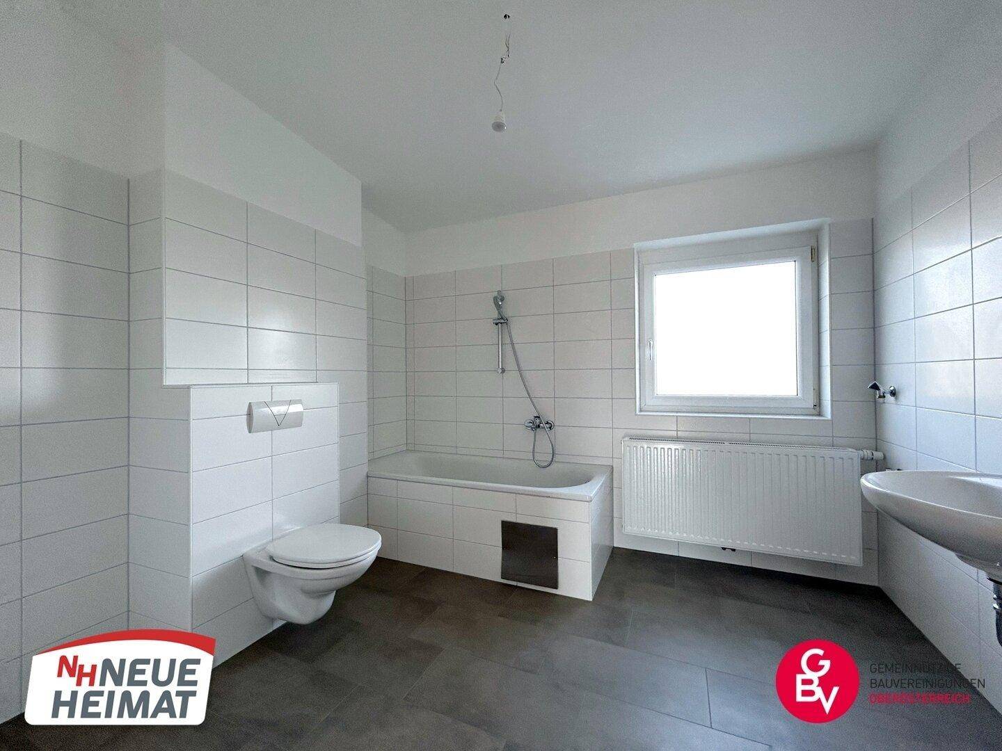 Modernes Badezimmer mit Badewanne, WC und Fenster, ausgestattet mit weißen Fliesen.