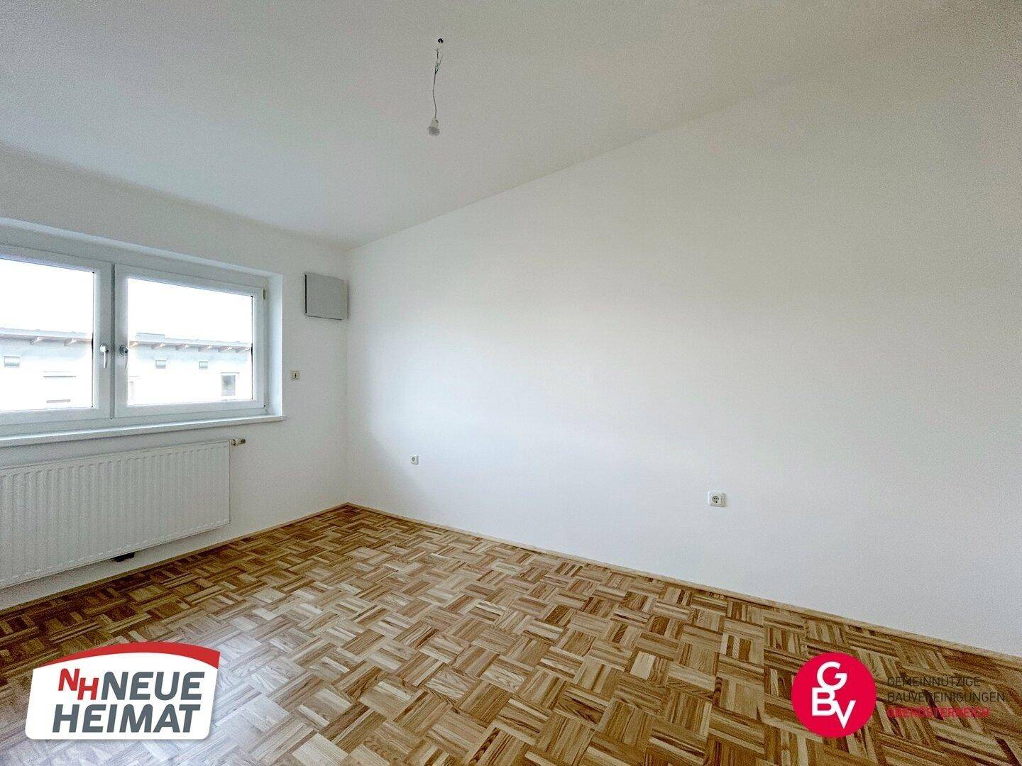 Helles Schlafzimmer mit Parkettboden und großem Fenster, bietet viel Tageslicht.