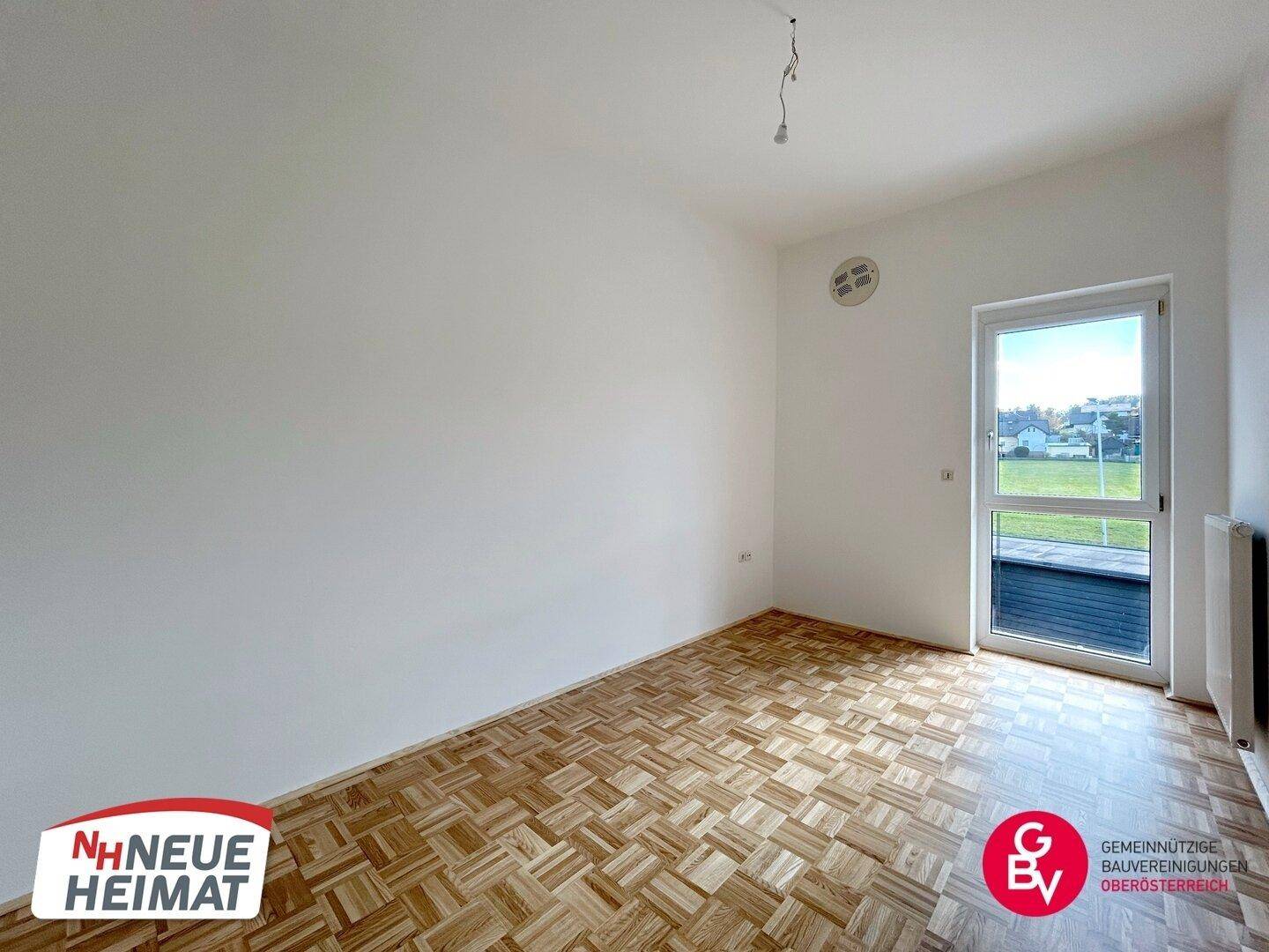 Geräumiges Zimmer mit Parkettboden und Tür zum Außenbereich, bietet viel Tageslicht.