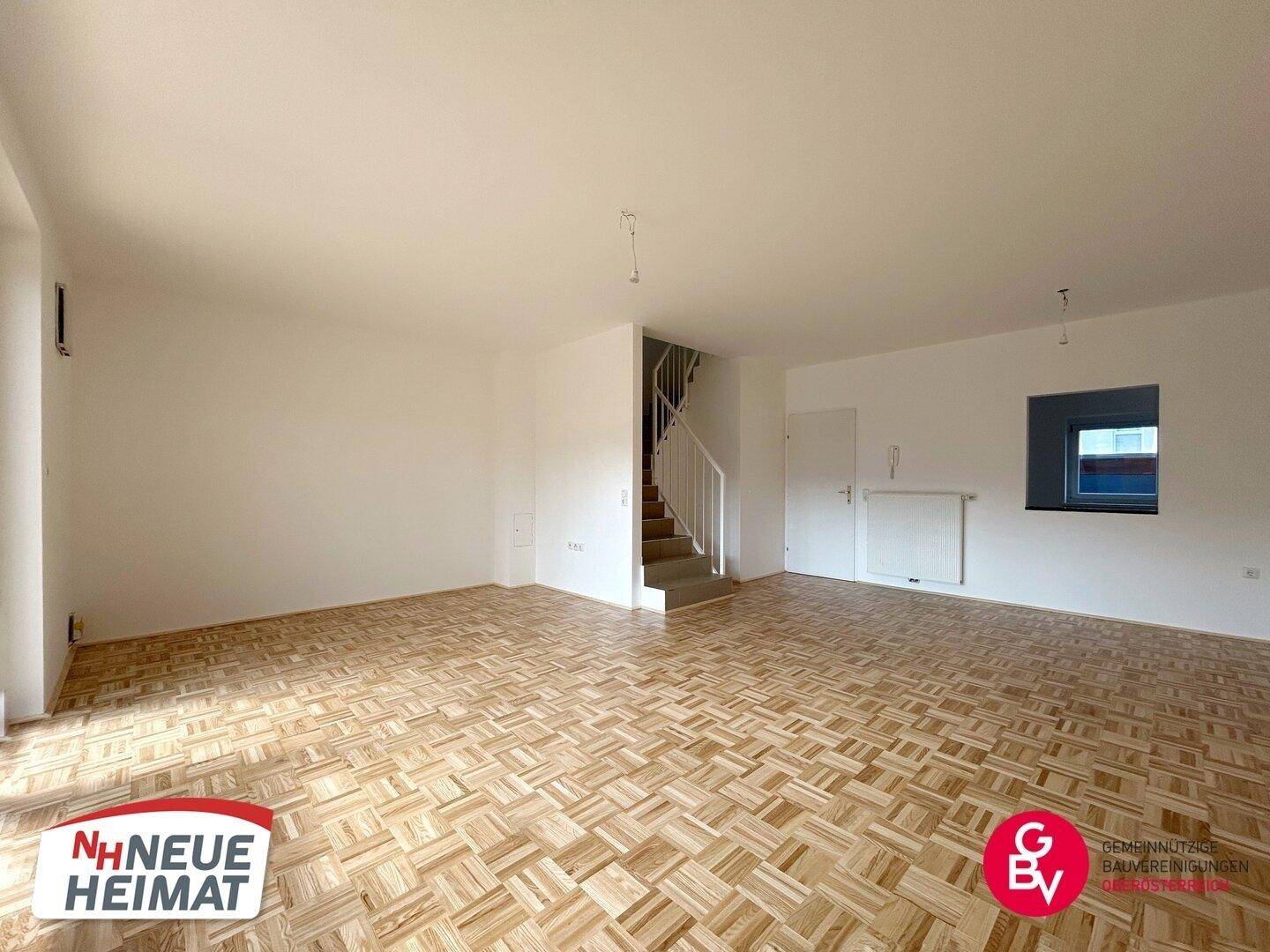 Großzügiges, leeres Wohnzimmer mit Parkettboden und Treppenaufgang, bietet viel Gestaltungsfreiheit.