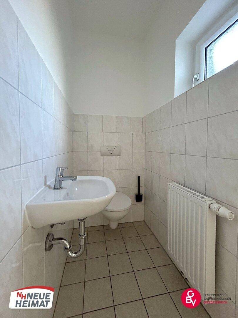 Kleines Gäste-WC mit Waschbecken, Toilette und Fenster, ausgestattet mit hellen Fliesen.