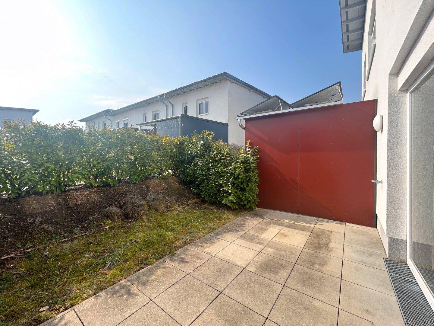 Gepflasterte Terrasse mit angrenzender Rasenfläche und Hecke, ideal für entspannte Stunden im Freien.
