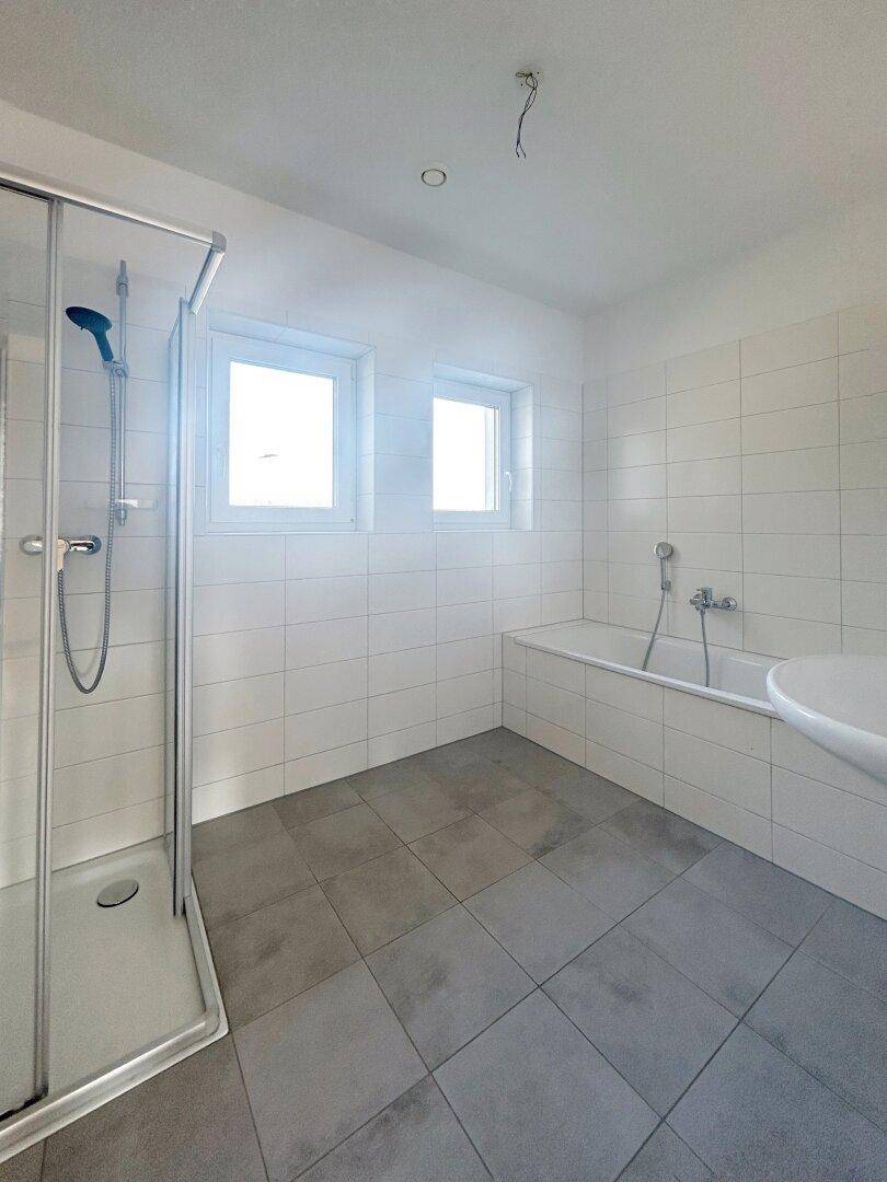 Modernes Badezimmer mit Duschkabine, Badewanne, Waschbecken und zwei Fenstern für Tageslicht.