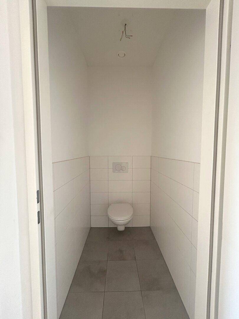 Separates Gäste-WC mit wandhängender Toilette und hellen Fliesen an Wänden und Boden.