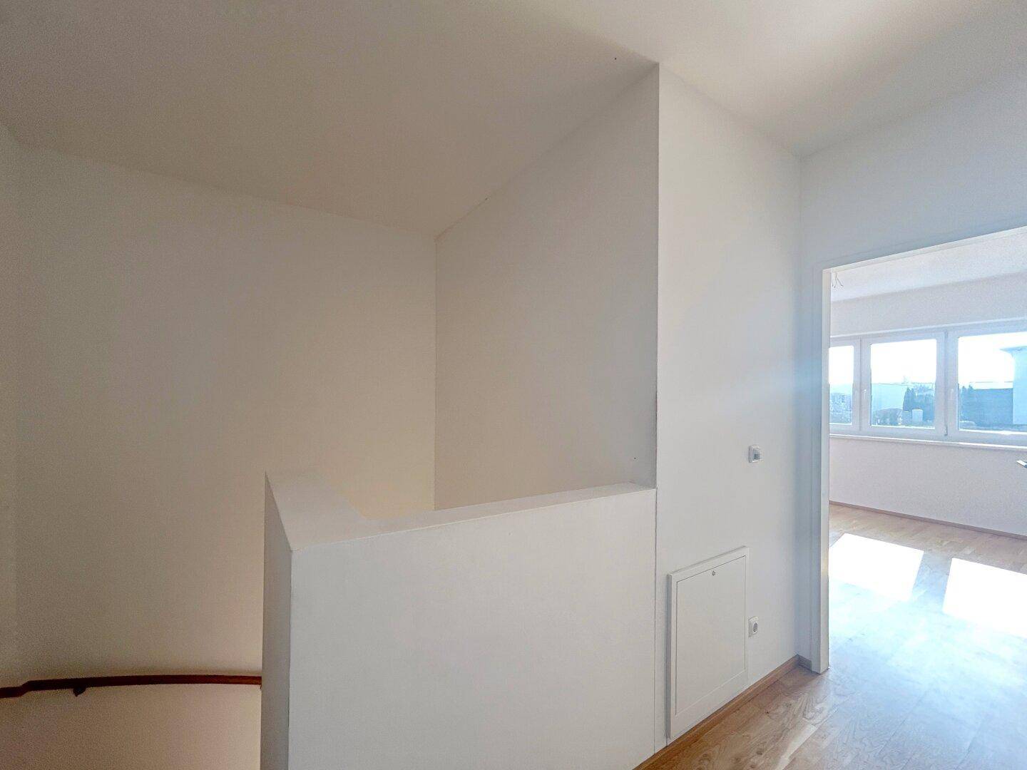 Heller Treppenabsatz im Obergeschoss mit Blick in ein angrenzendes Zimmer mit großen Fenstern.