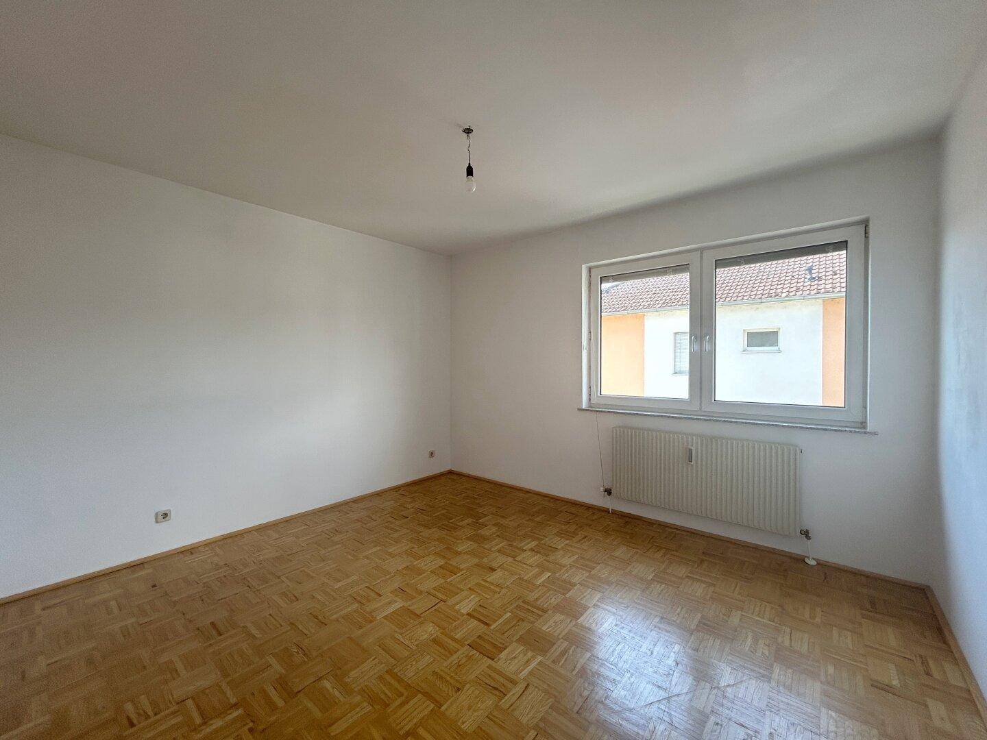Leeres Zimmer mit Parkettboden und Fenster, gut geeignet als Schlafzimmer oder Büro.