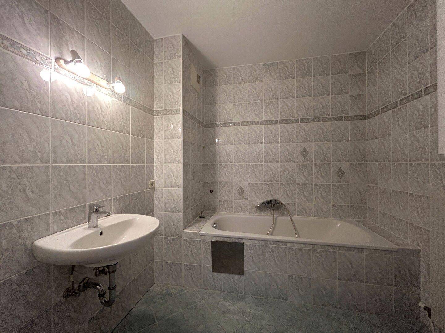 Gefliestes Badezimmer mit Badewanne und Waschbecken, in einem älteren Stil gehalten.