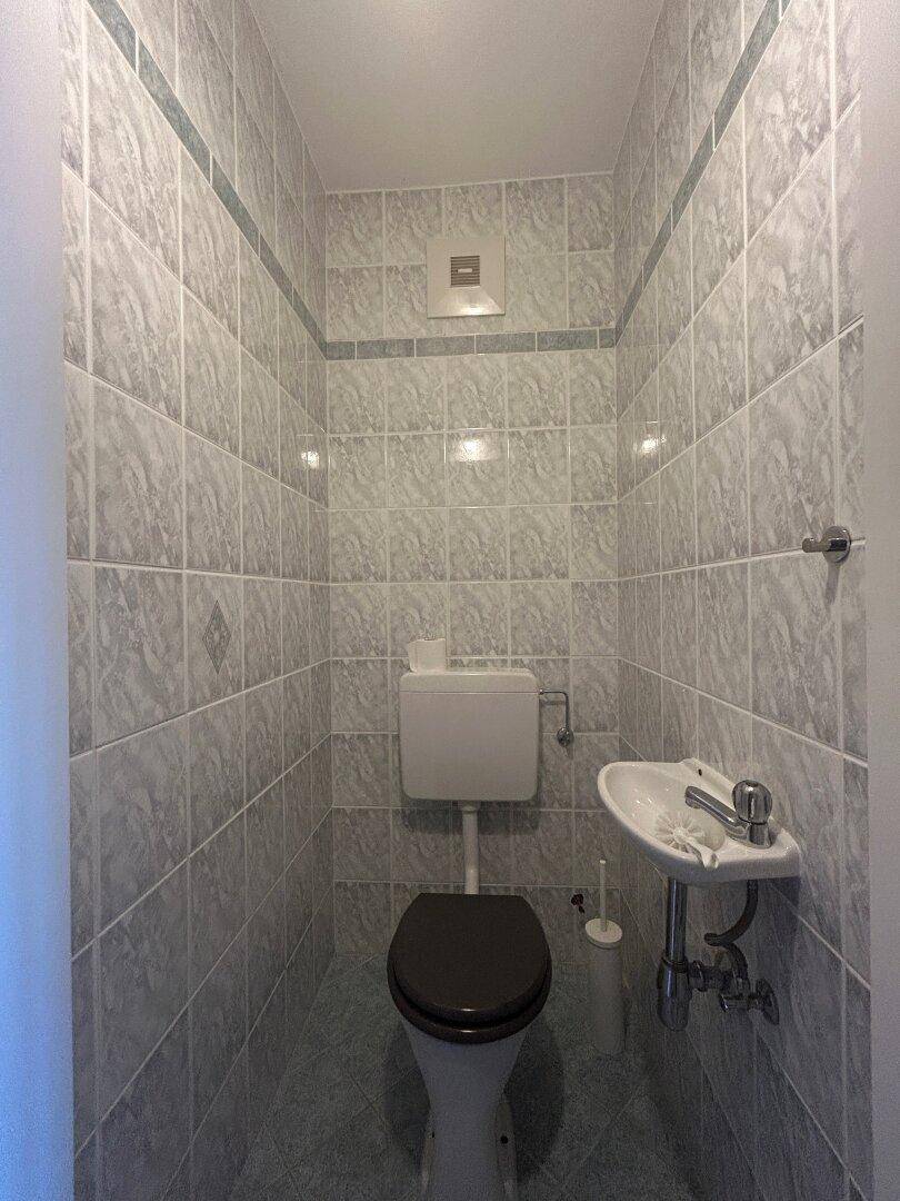 Kleines Gäste-WC mit Fliesen an Wänden und Boden, ausgestattet mit Toilette und Waschbecken.