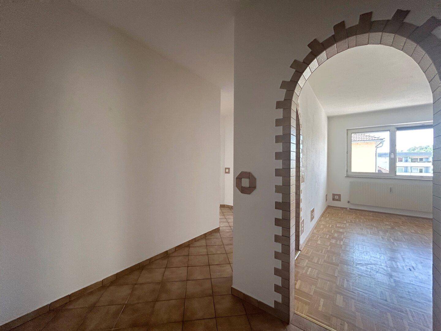 Flur mit Fliesenboden und einem dekorativen Ziegelbogen, der den Übergang zu einem Zimmer markiert.
