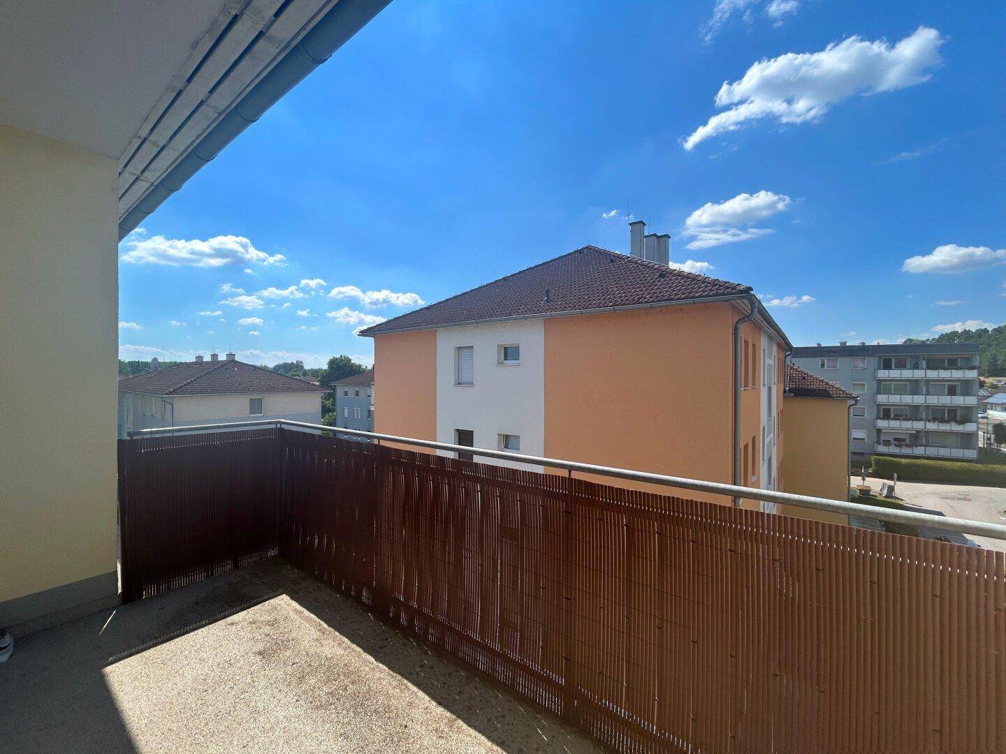 Sonniger Balkon mit Blick auf die umliegenden Gebäude und die grüne Landschaft.