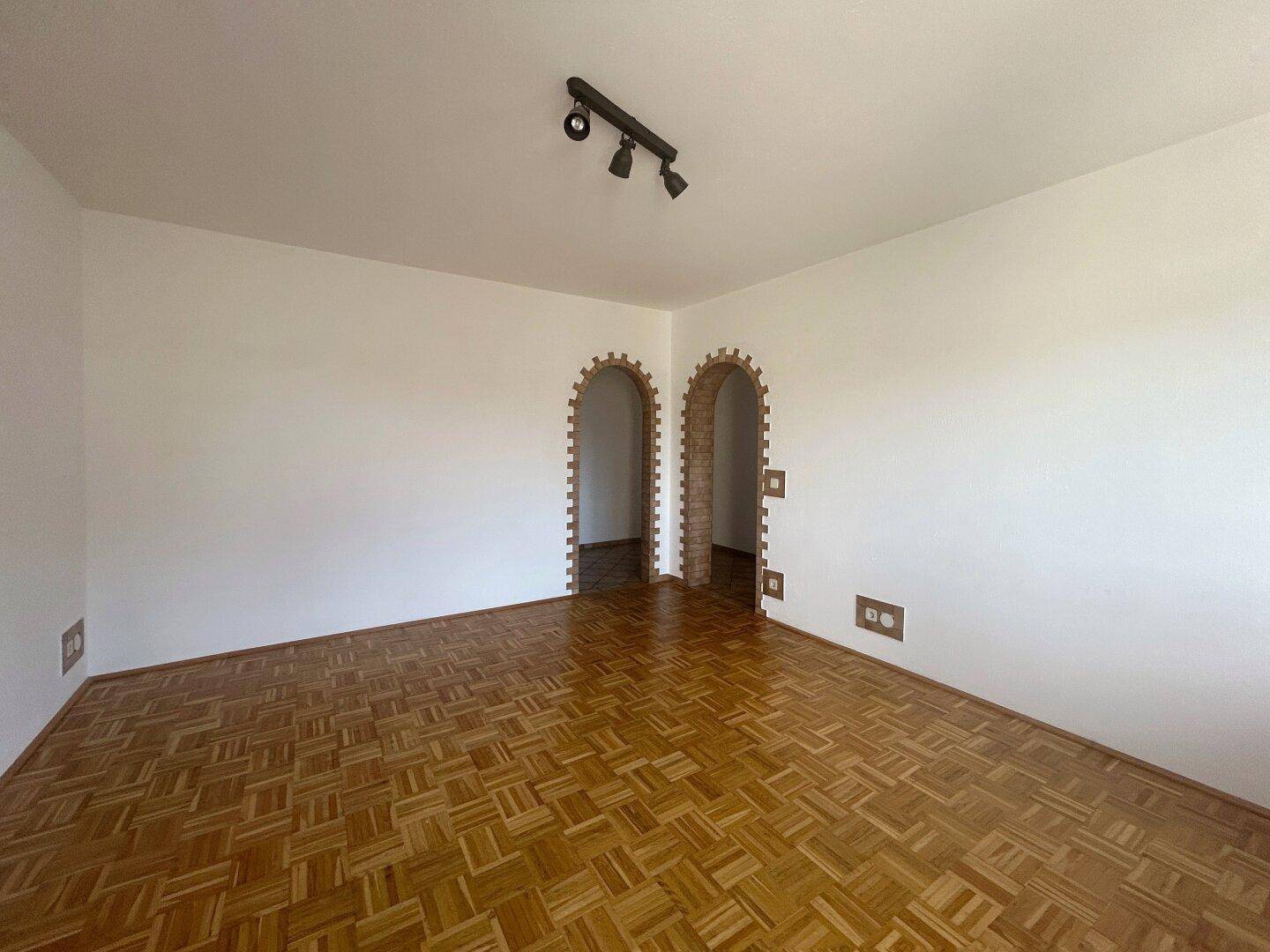Geräumiges Zimmer mit Parkettboden und zwei dekorativen Ziegelbögen, ideal als Wohnzimmer.