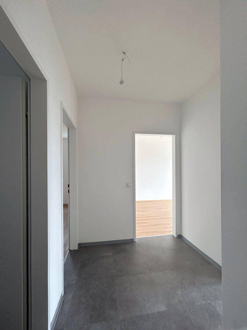 Heller Flur mit dunklem Fliesenboden und weißen Wänden, der zu verschiedenen Räumen der Wohnung führt.