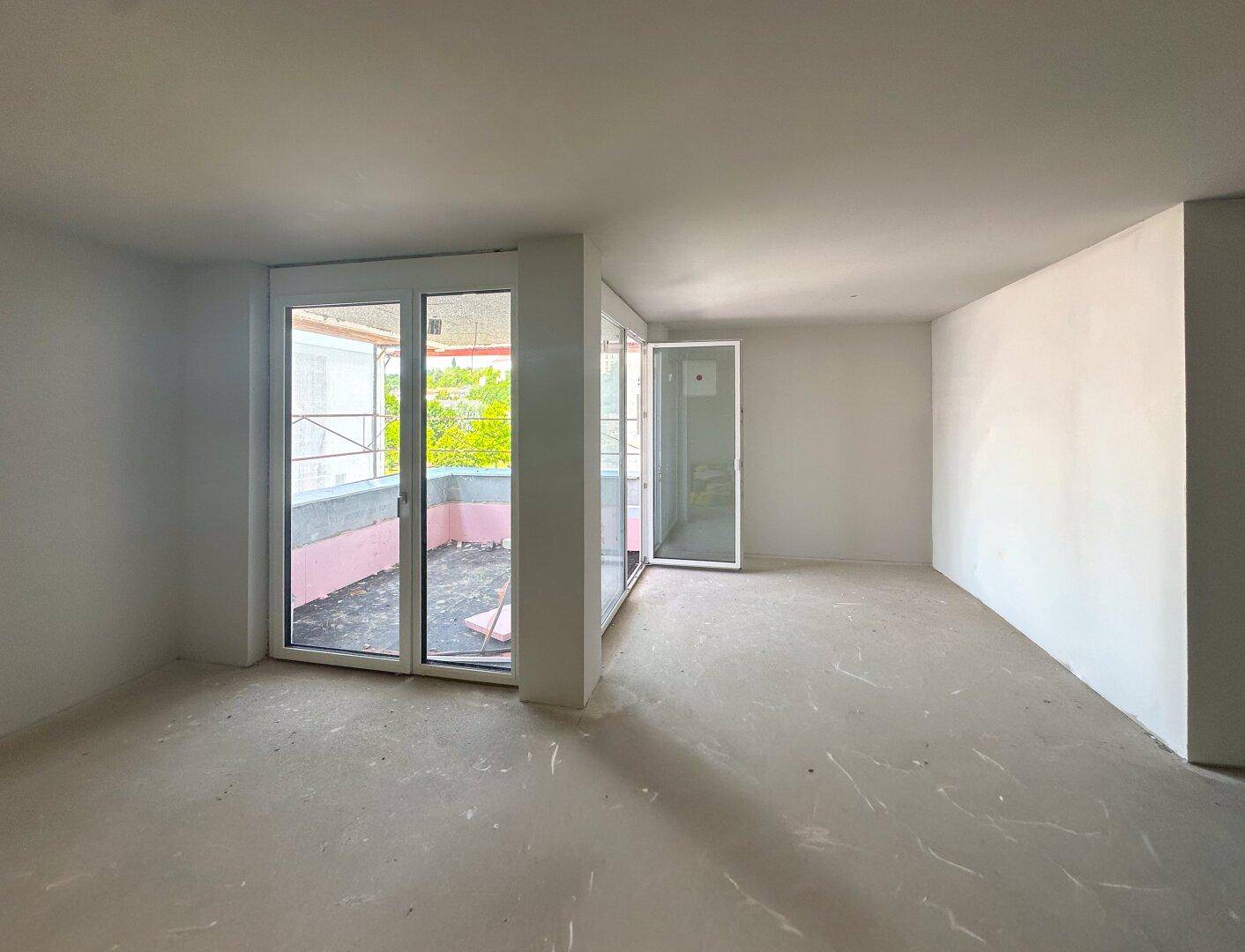 Unfertiger Wohnbereich mit großen Fenstern und direktem Zugang zu einem Balkon.