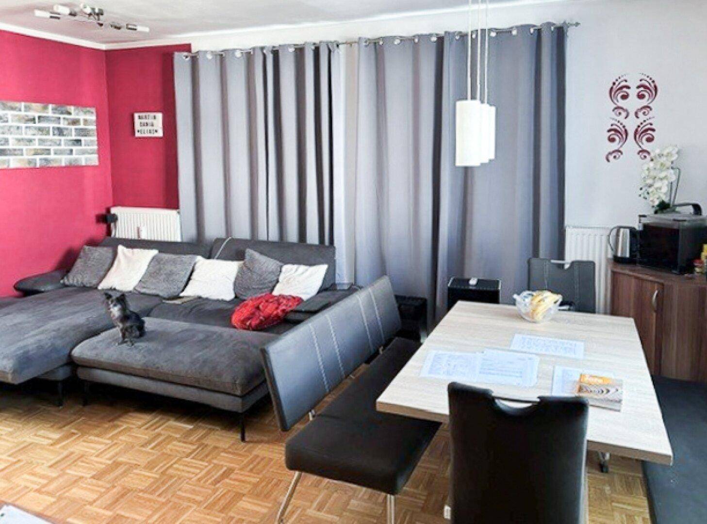 Gemütlicher Wohn-Essbereich mit großem Ecksofa, Esstisch und farbigen Wänden.