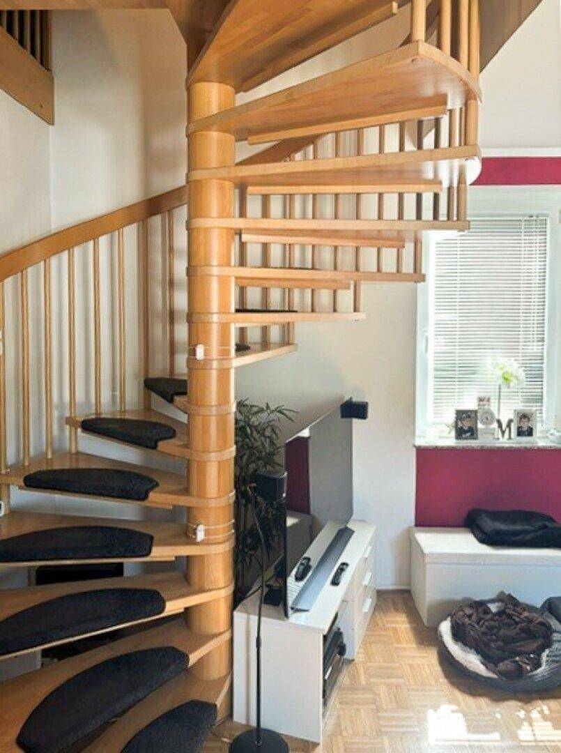 Elegante Holz-Wendeltreppe in einem Wohnbereich mit Parkettboden und Fenster.
