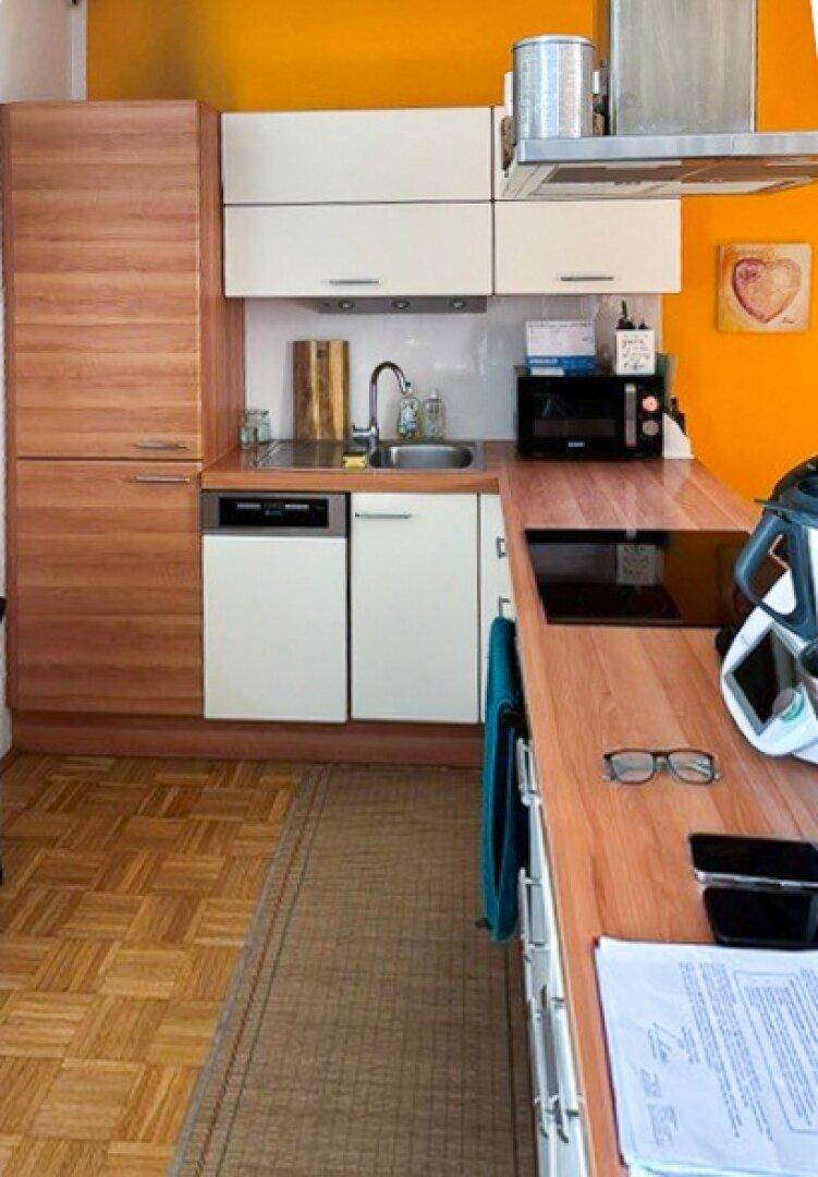 Kompakte Küche mit Holzfronten, Arbeitsplatte und einer auffälligen orangefarbenen Wand.