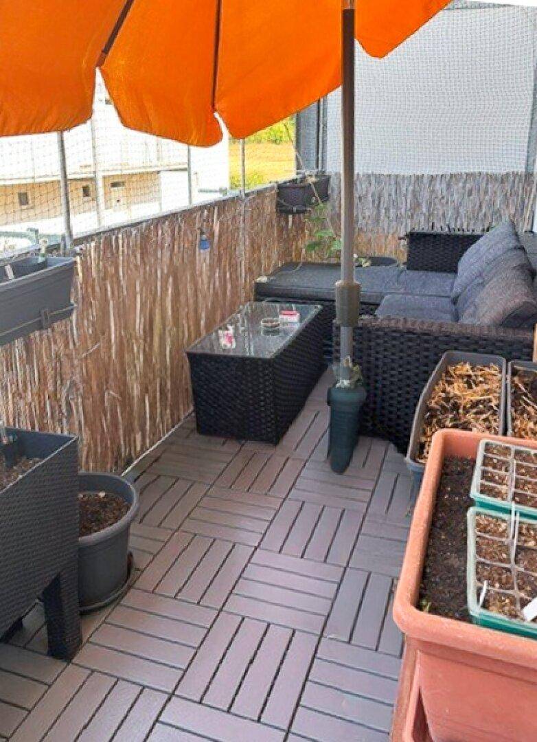 Gemütlicher Balkon mit Outdoor-Möbeln, Sonnenschirm und Pflanzen in Töpfen.