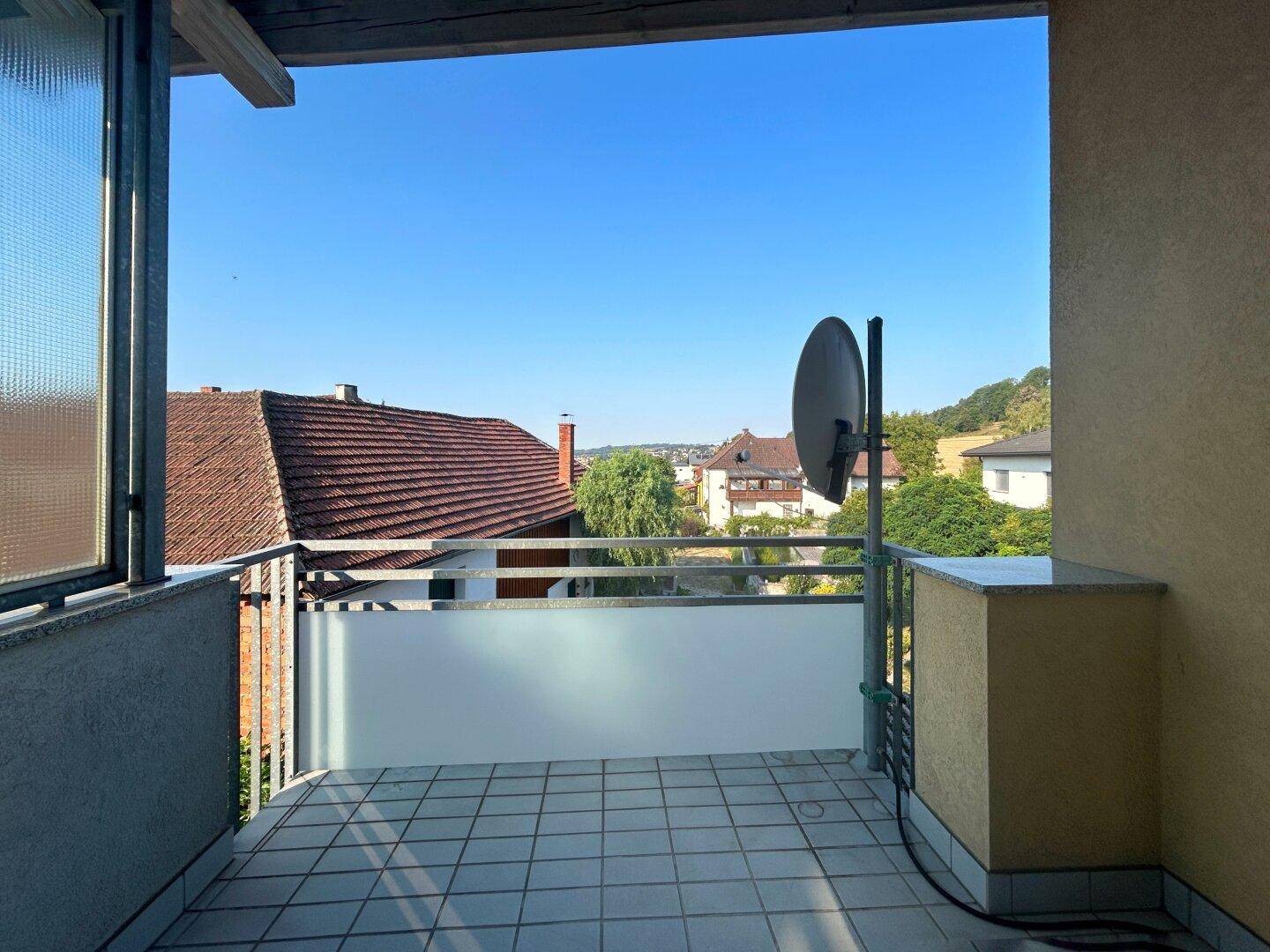 Sonniger Balkon mit Fliesenboden und Blick über die Dächer der Umgebung.