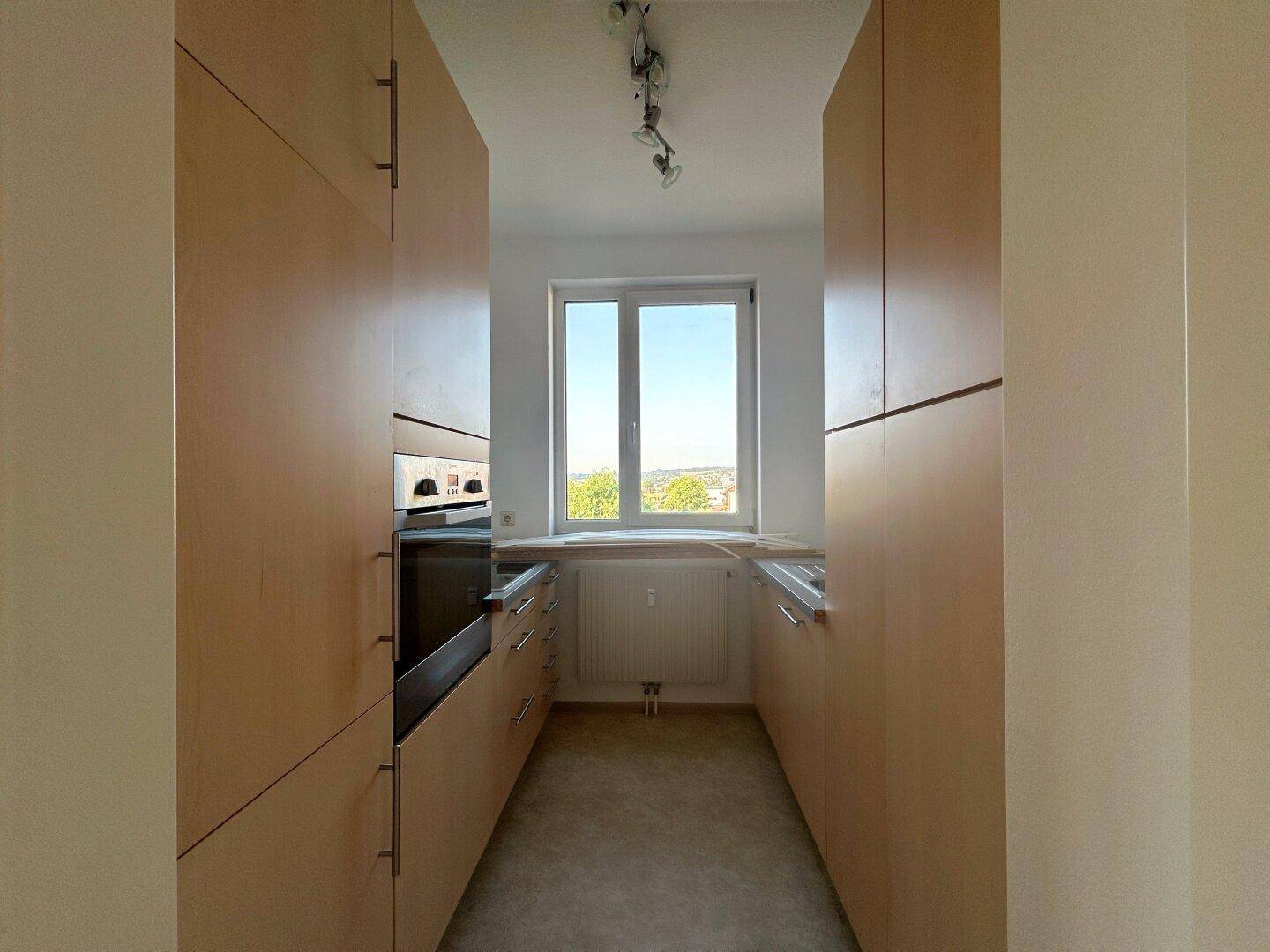 Funktionale Küche mit hellen Holzschränken, Einbauofen und Fenster mit Ausblick.